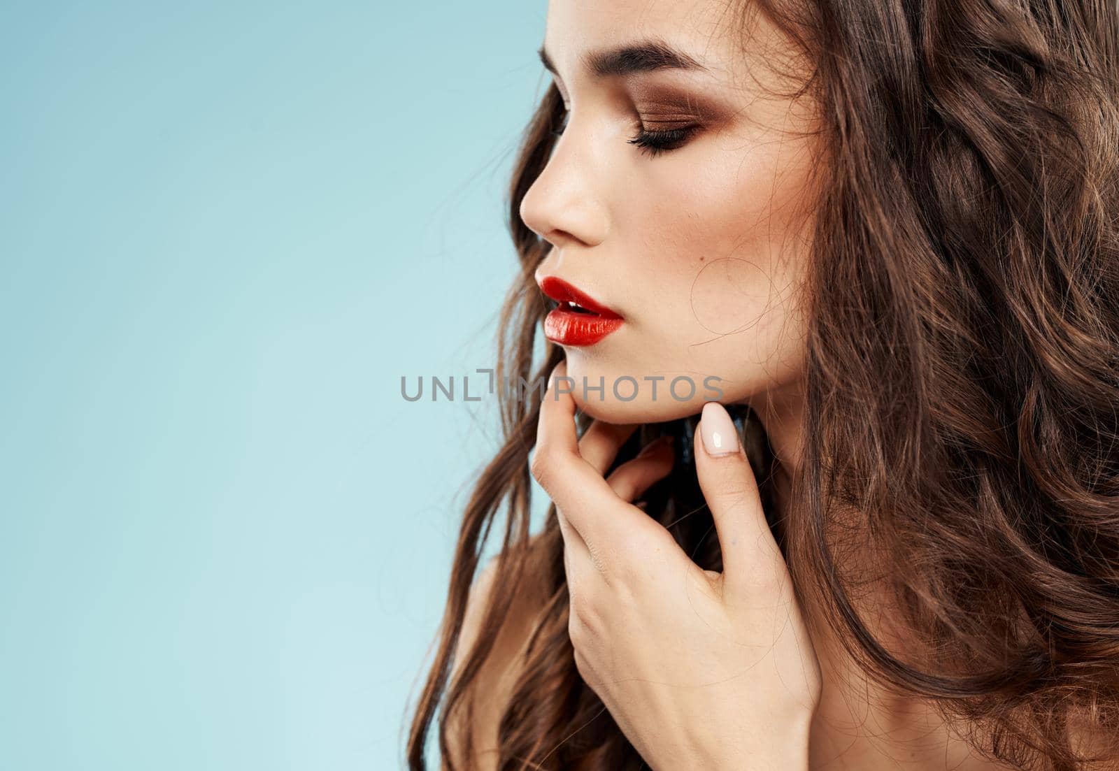 Beautiful woman model holds her finger near the face on a blue background and curly hair. High quality photo