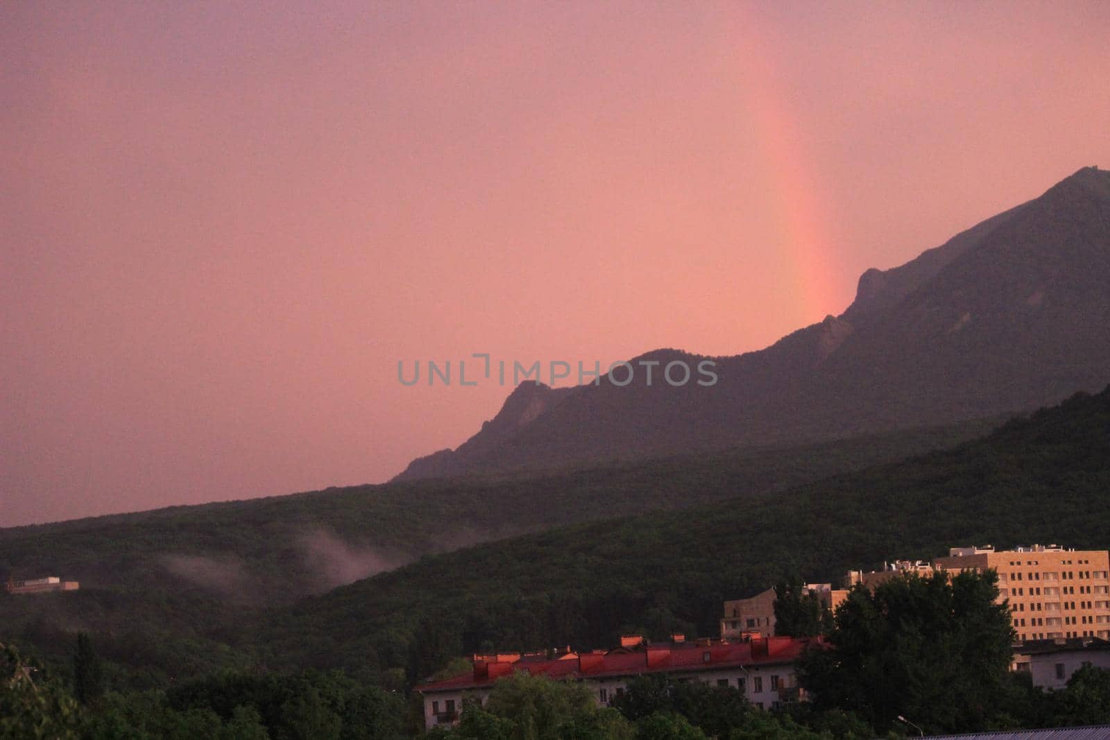 Rainbow over the city at sunset. Mountain landscape with a rainbow. Vertical image.