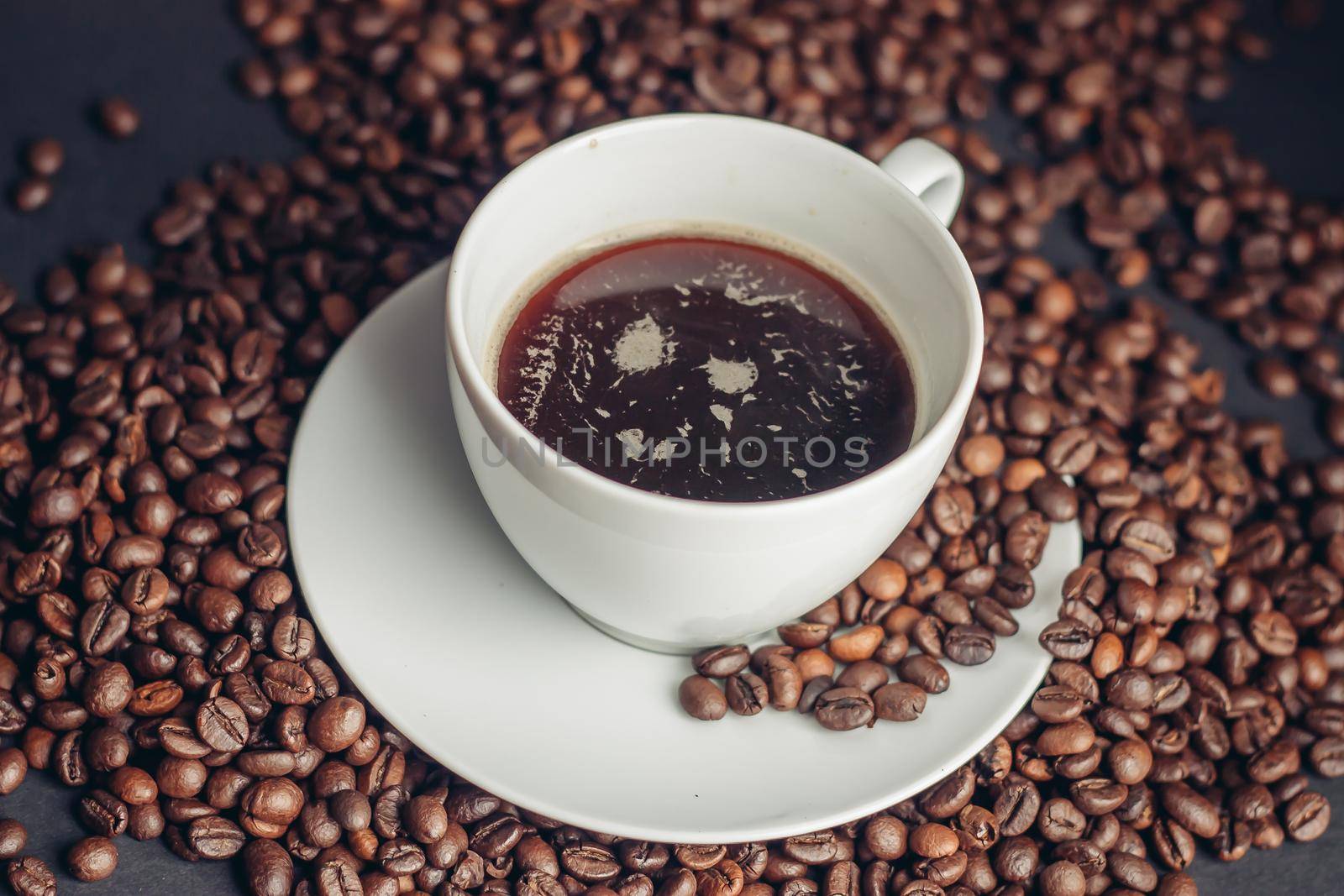 coffee beans and a cup on a white saucer dark background drink. High quality photo
