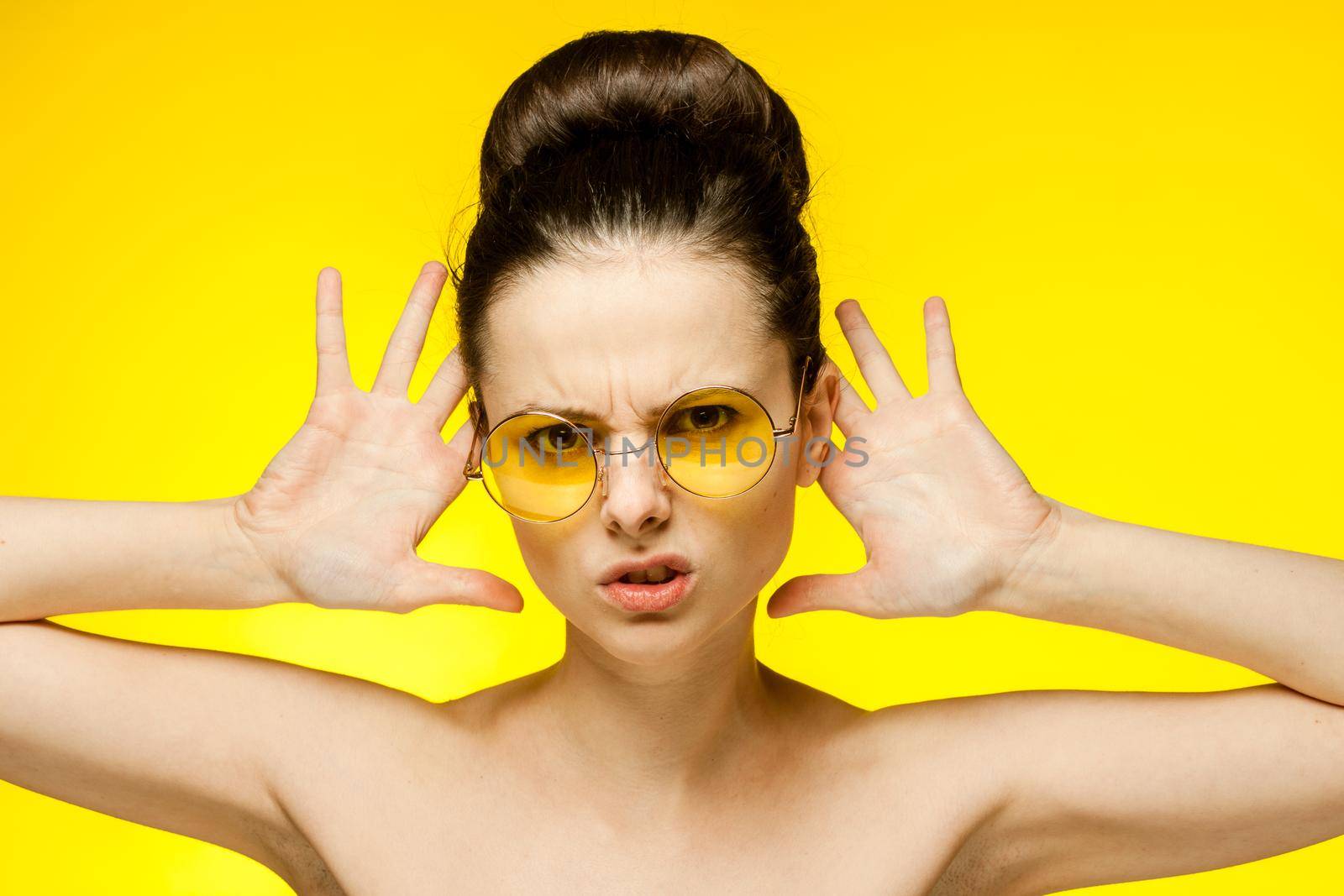 woman with bare shoulders yellow glasses hands near face clear skin. High quality photo