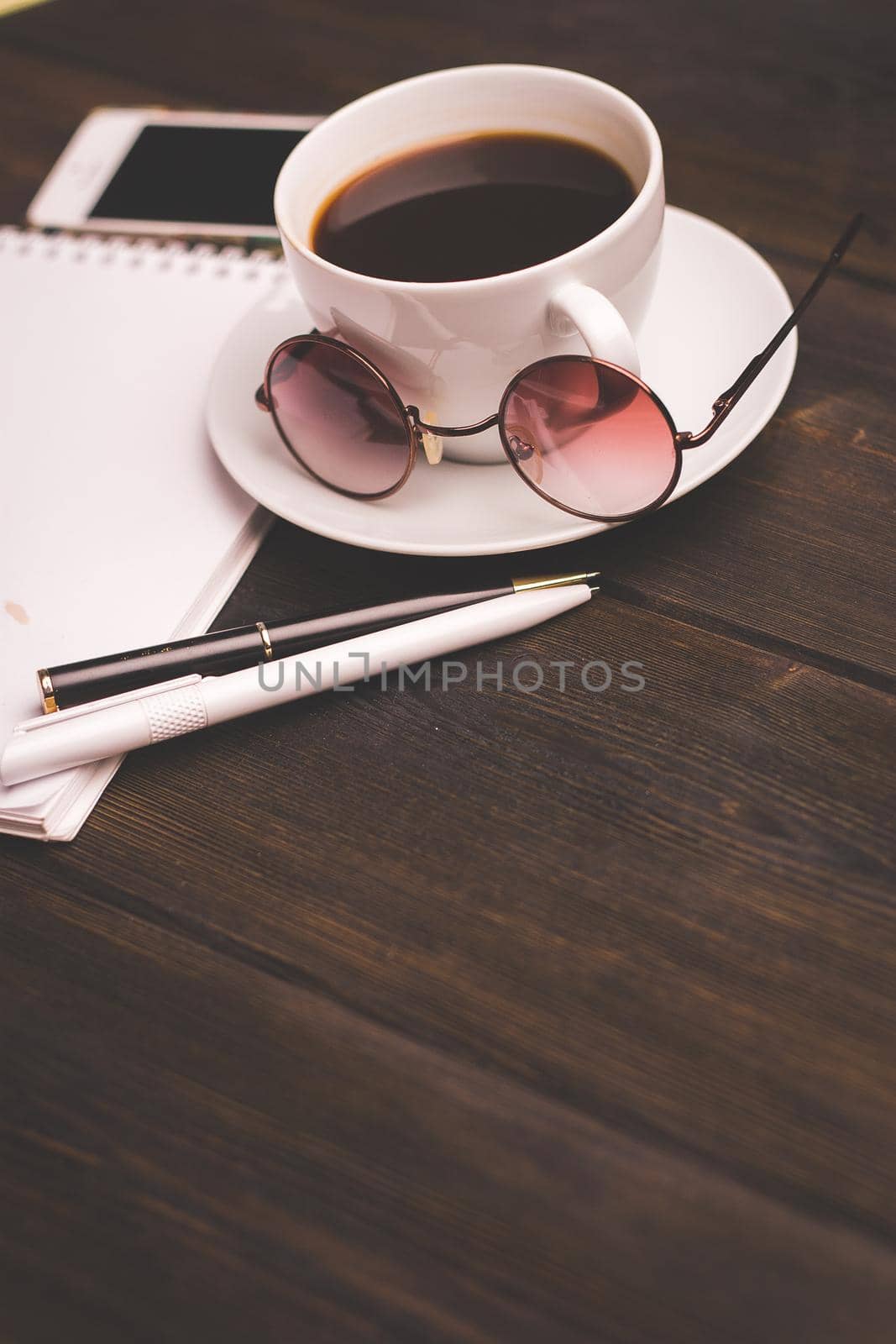 cup of coffee on a saucer wooden table notepad pen office stationery by SHOTPRIME