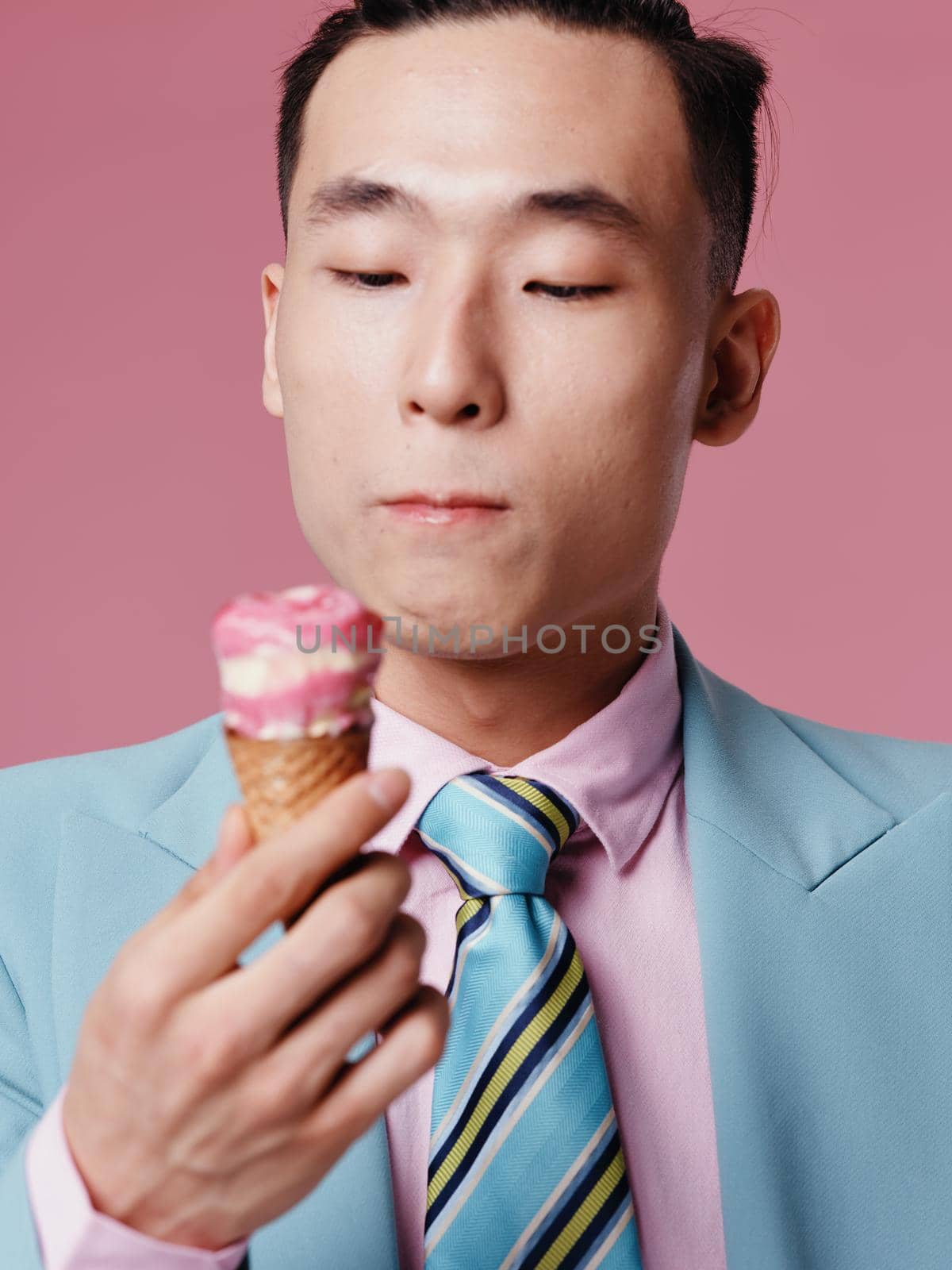 Handsome Asian man in blue jacket with ice cream in hand on pink background. High quality photo
