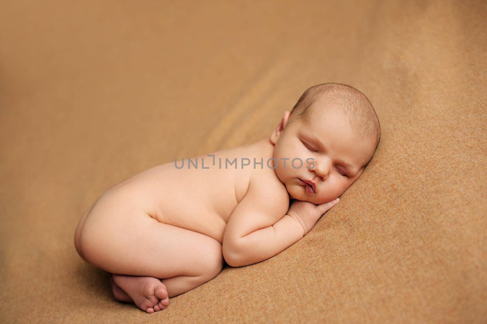 Newborn baby posed on a beige blanket with her hands under her cheeks at a newborn photo shoot