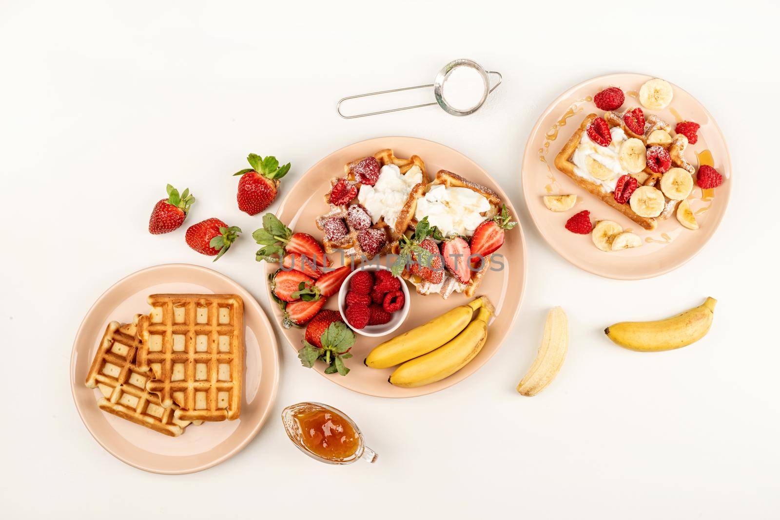 Homemade waffles with fruits and berries, cream and honey in a plate on white table. Flat lay, top view, copy space.