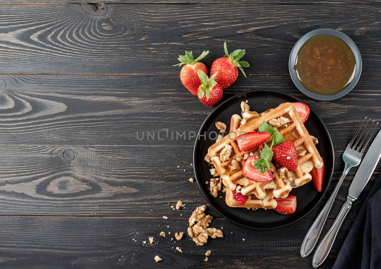 Flat lay of black plate with Belgian waffles with fresh stawberry on dark wooden background. Flat lay, top view copy space.