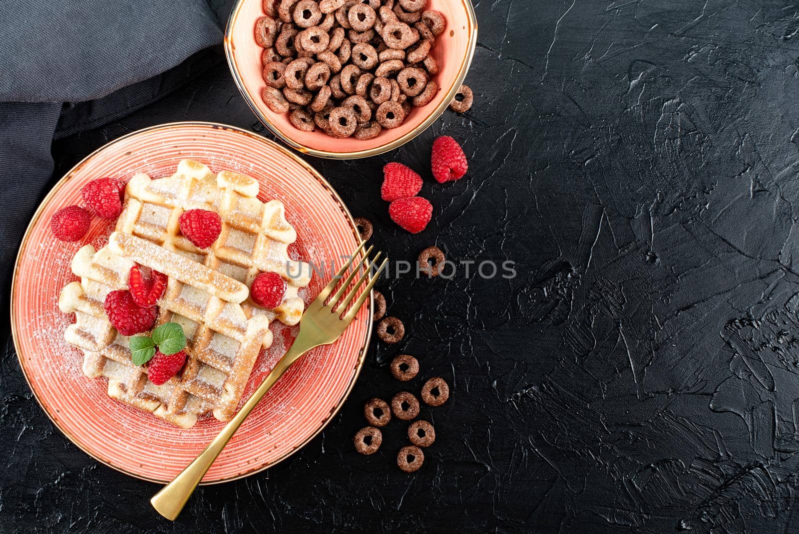 breakfast with waffles and a bowl of chocolate cereal on black backgrownd. Flat lay, top view, copy space.