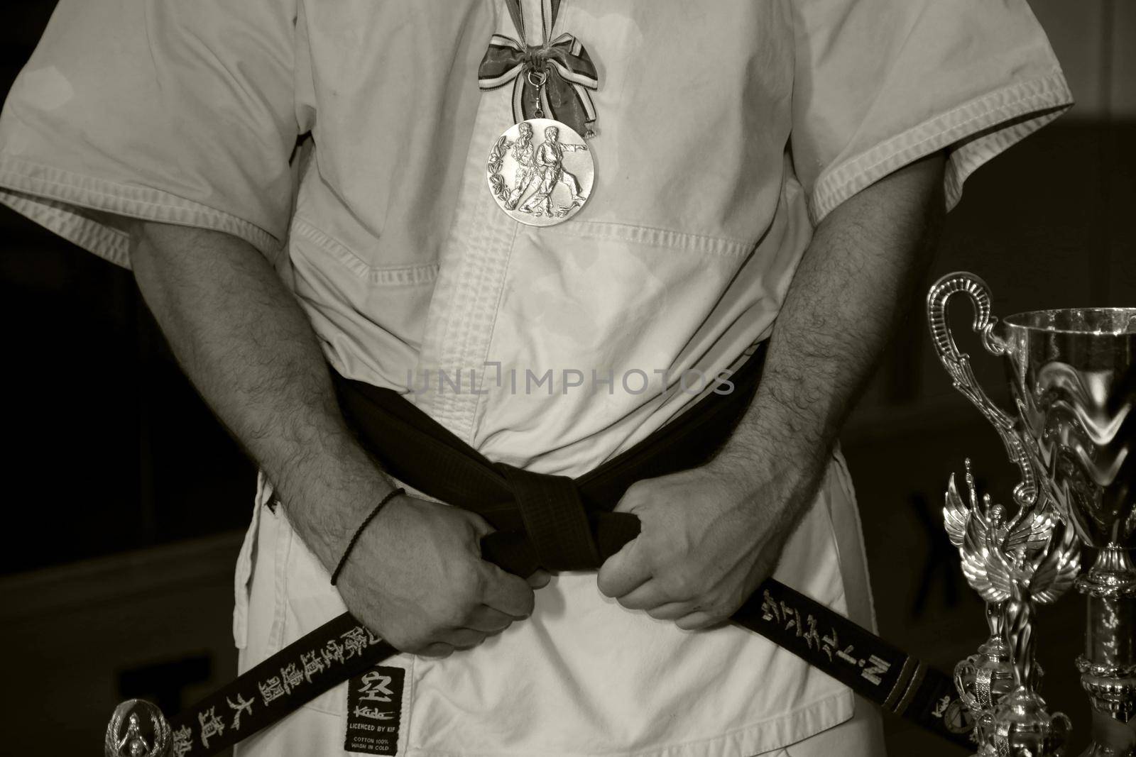 Variety and martial arts.Champion in a white kimono with a black belt with a medal, and a cup. Black and white image.
