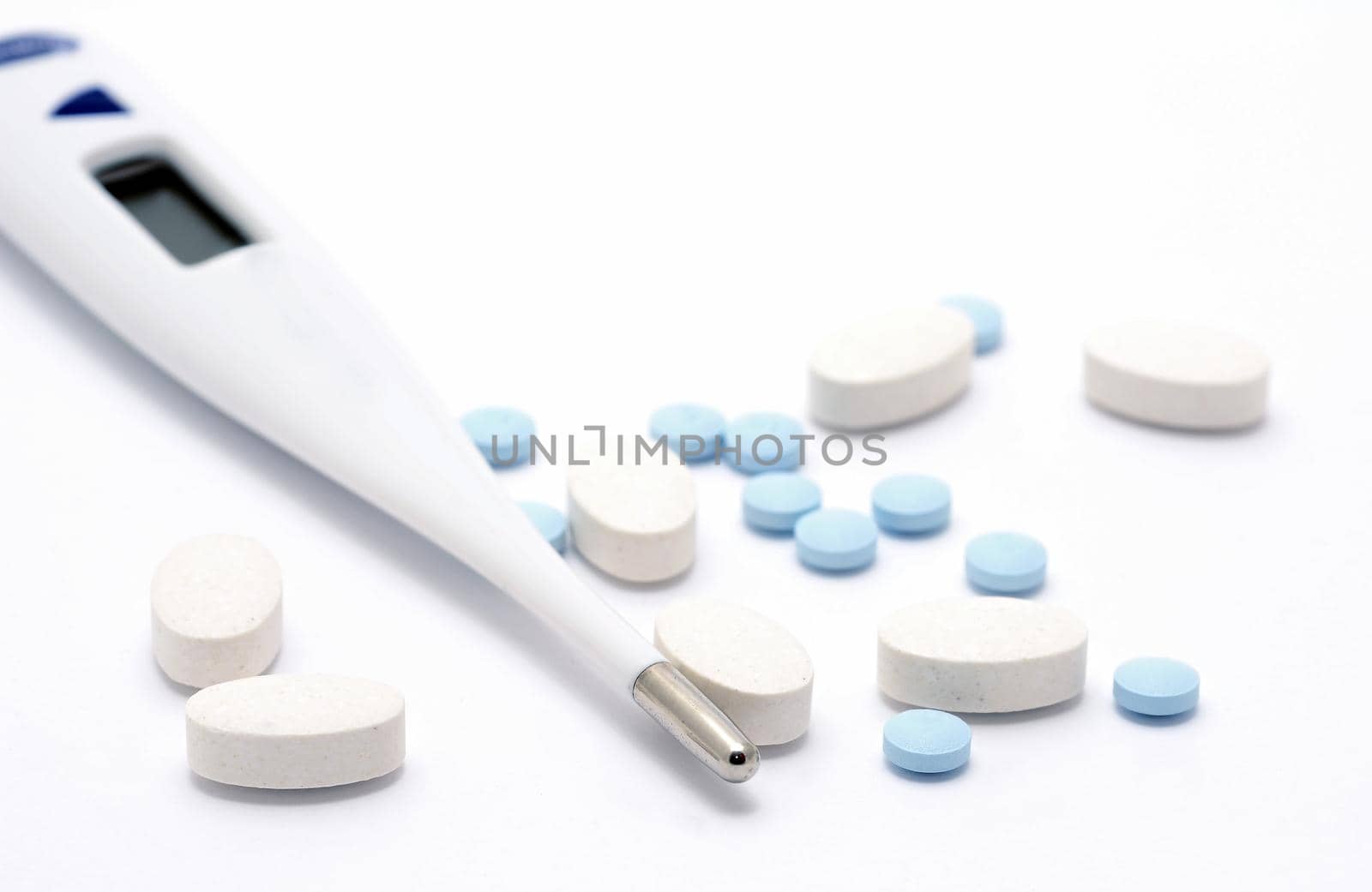 A close up of group of pills with thermometer on white background.