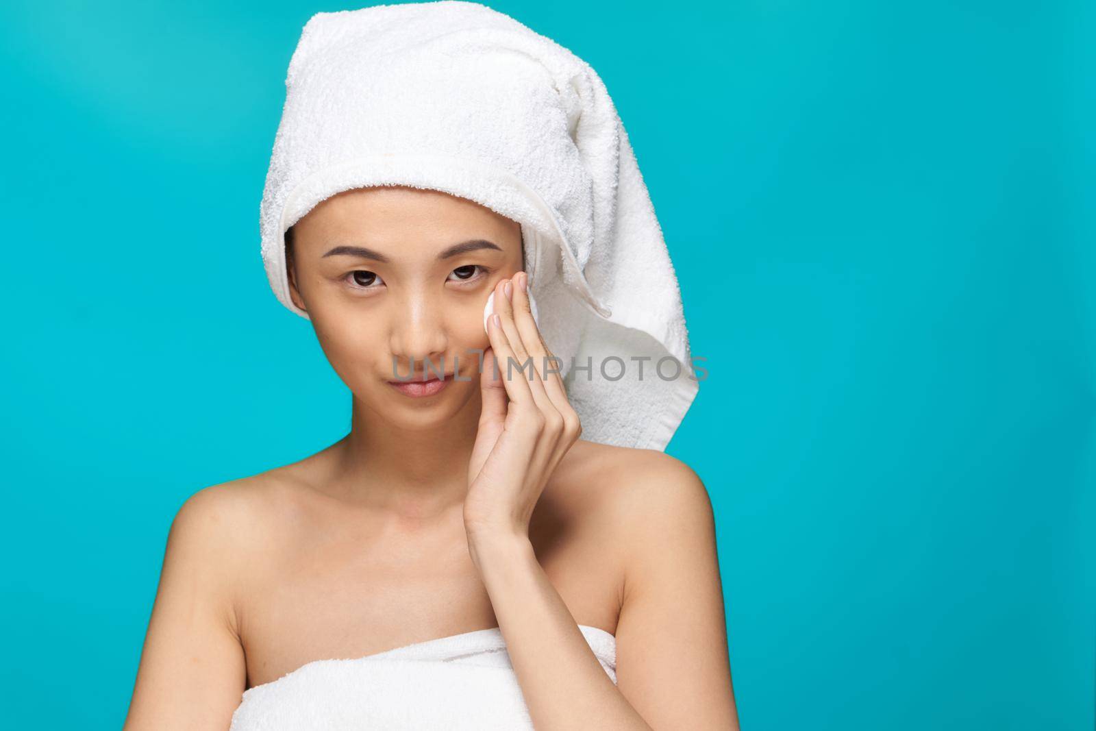 woman of asian appearance naked shoulders clear skin cotton pad blue background. High quality photo