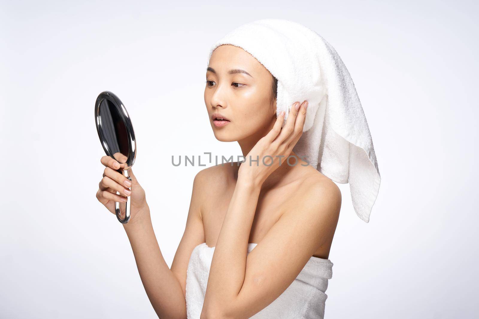 beautiful woman of asian appearance looks in the mirror with a towel on her head for spa treatments. High quality photo