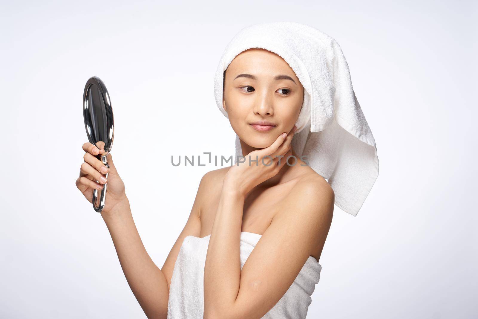 beautiful woman of asian appearance looks in the mirror with a towel on her head for spa treatments. High quality photo