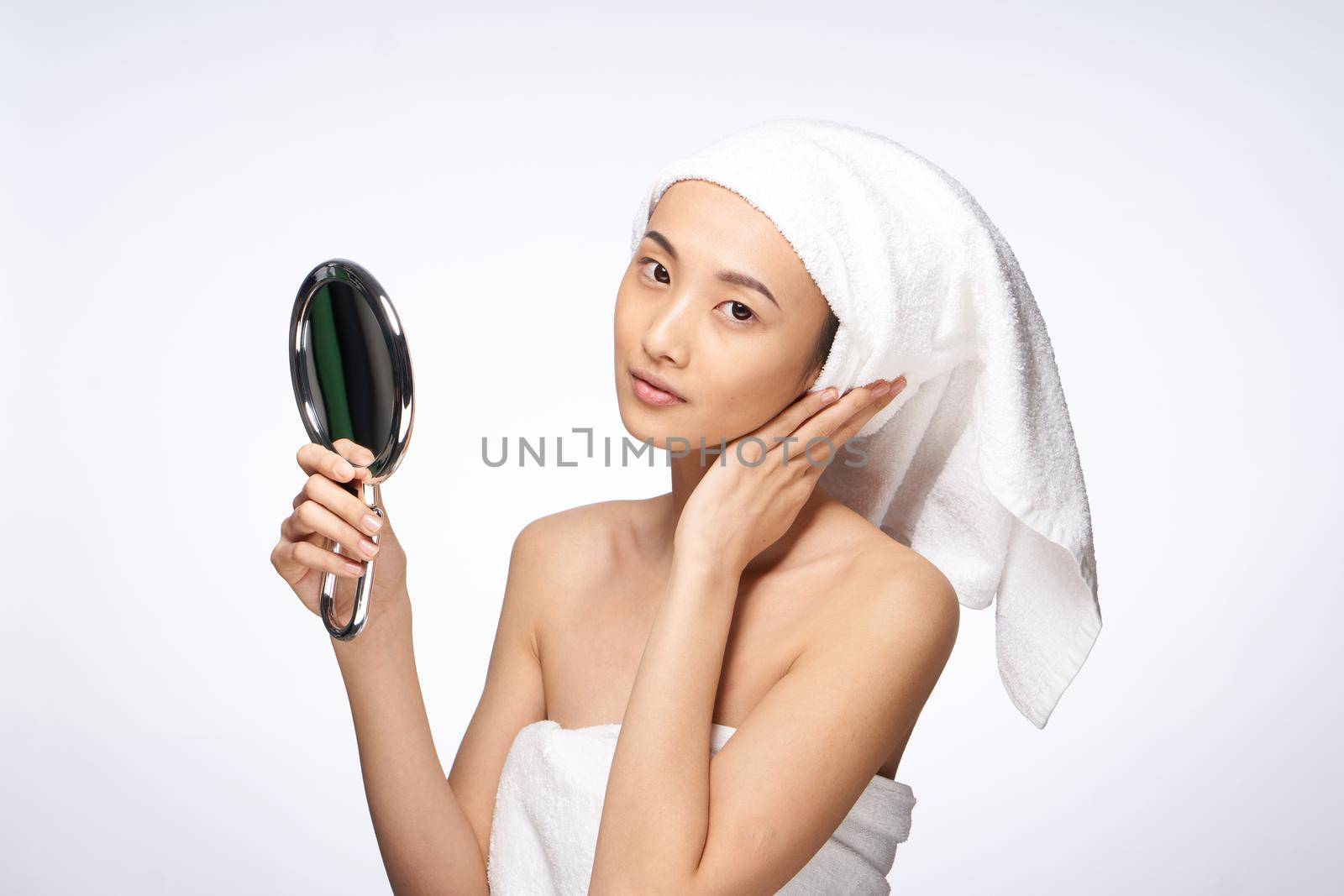 beautiful woman of asian appearance looks in the mirror with a towel on her head for spa treatments. High quality photo