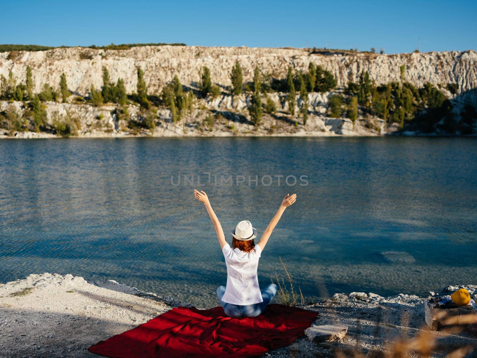 A woman sits on a red cloth near the river and a hat on her head. High quality photo
