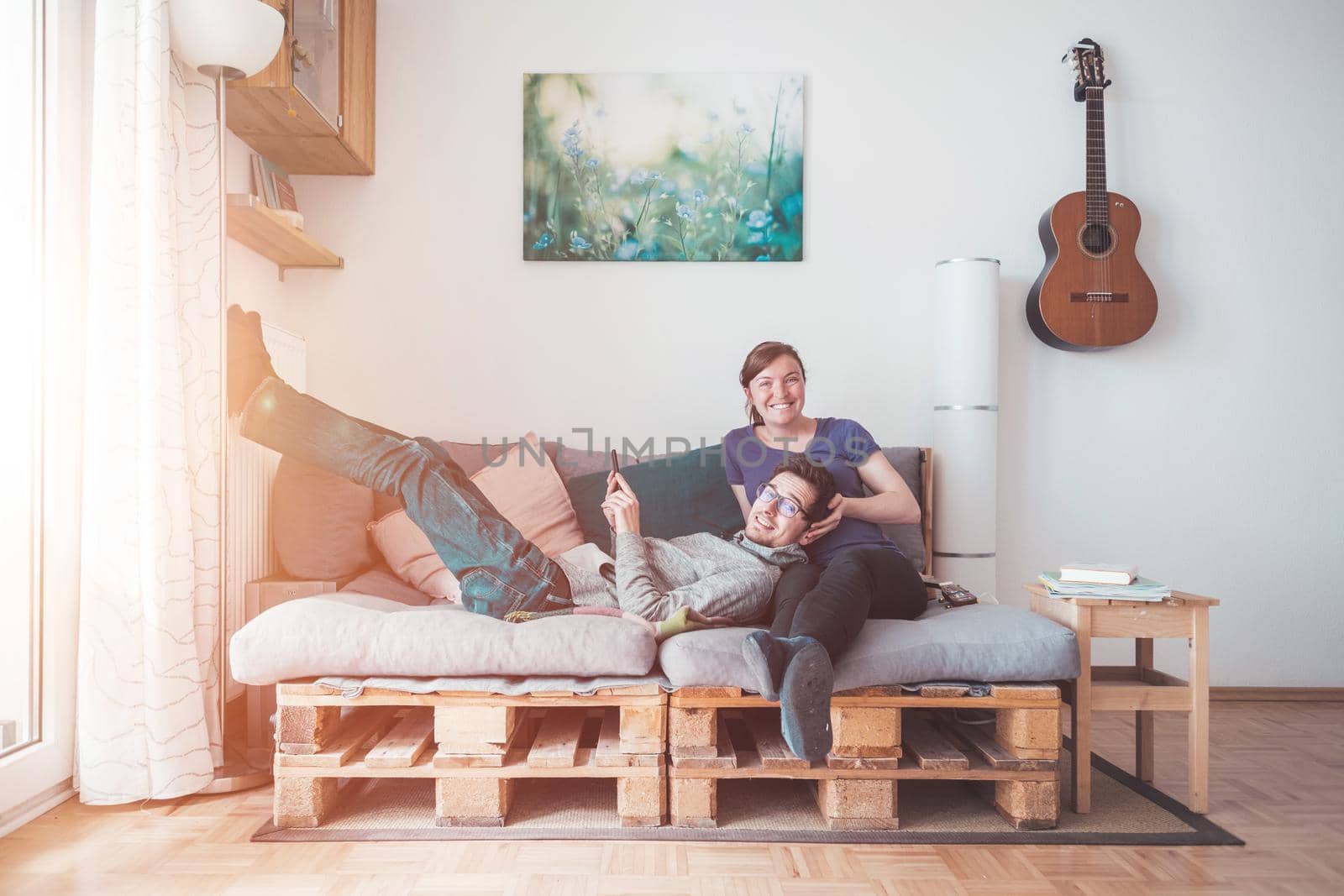 Young woman and man sitting on cozy palette sofa, living room