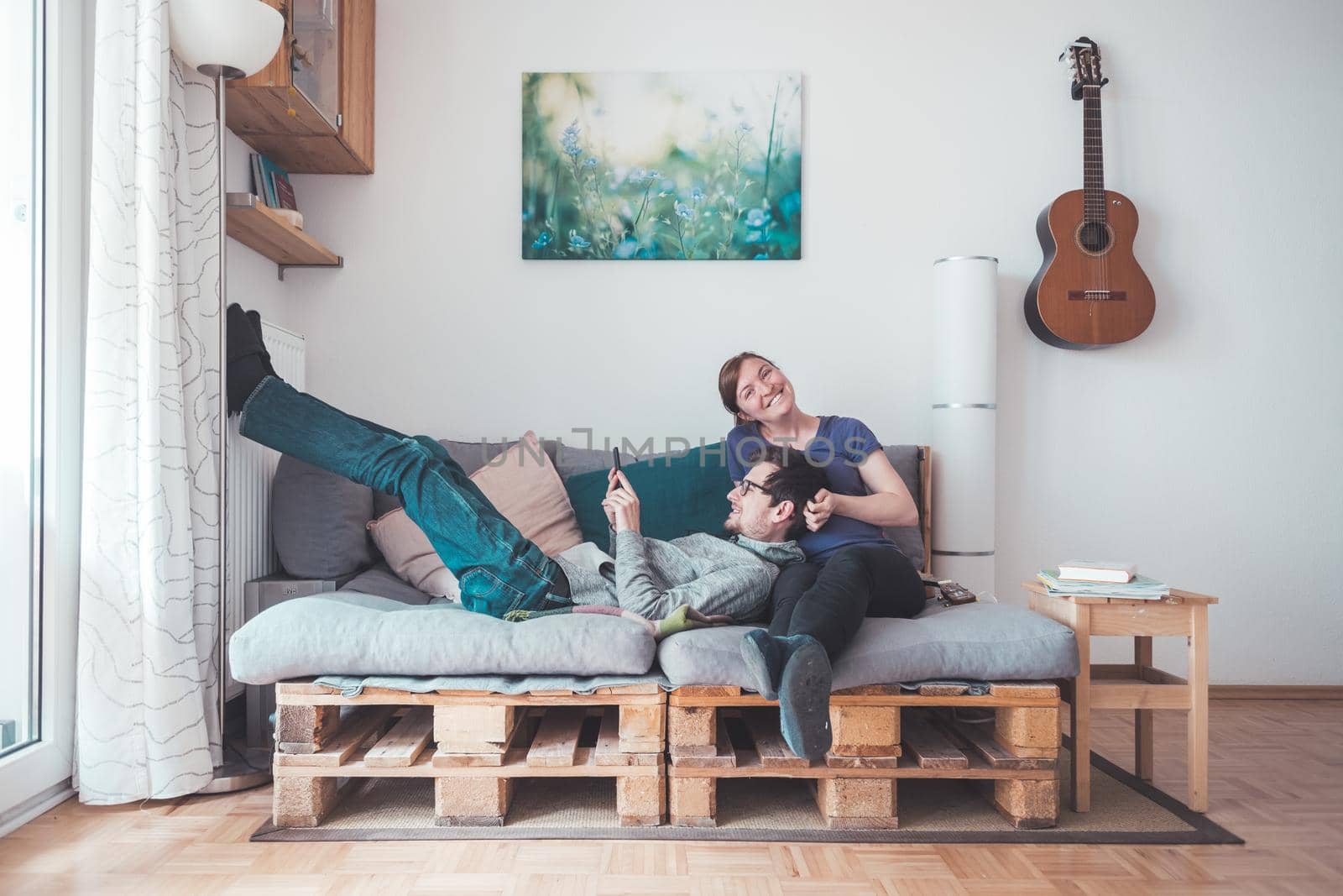 Young woman and man sitting on cozy palette sofa, living room