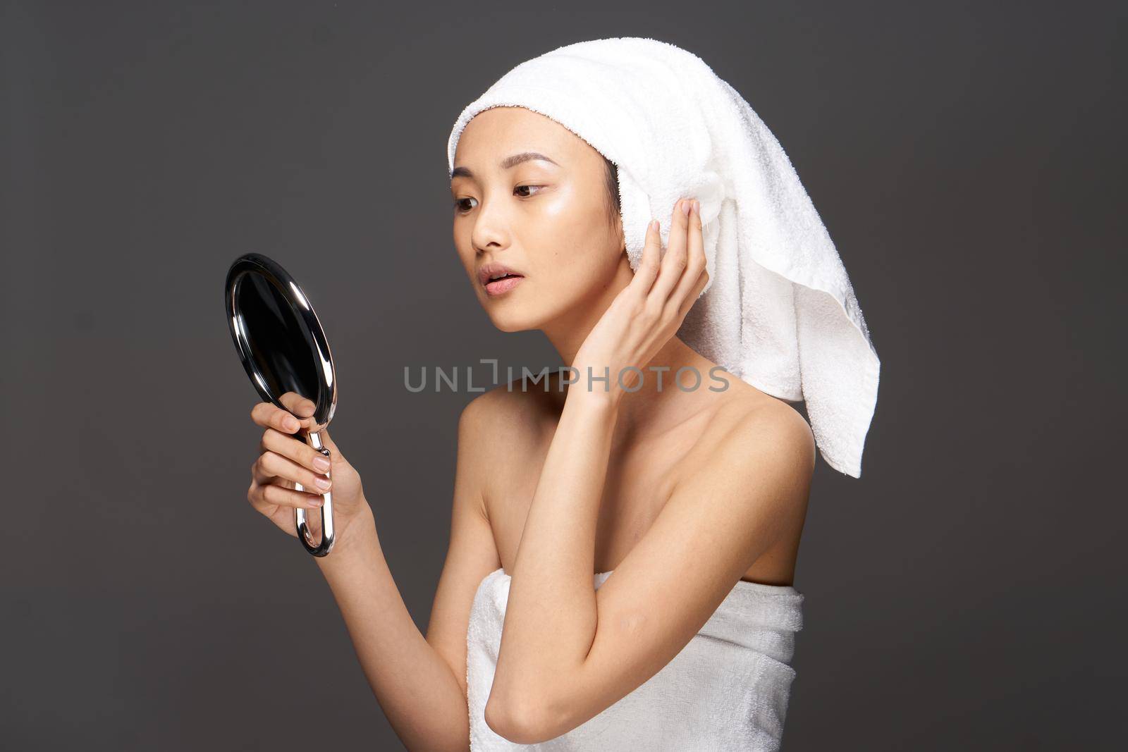 beautiful woman of asian appearance looks in the mirror with a towel on her head for spa treatments. High quality photo