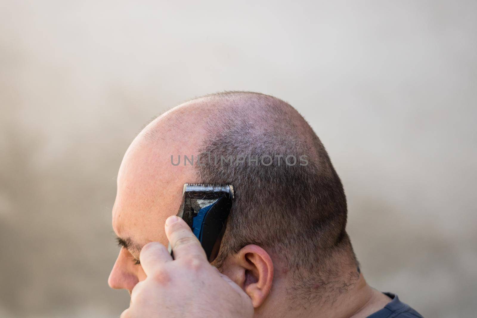 Male shaving or trimming his hair using a hair clipper or electric razor