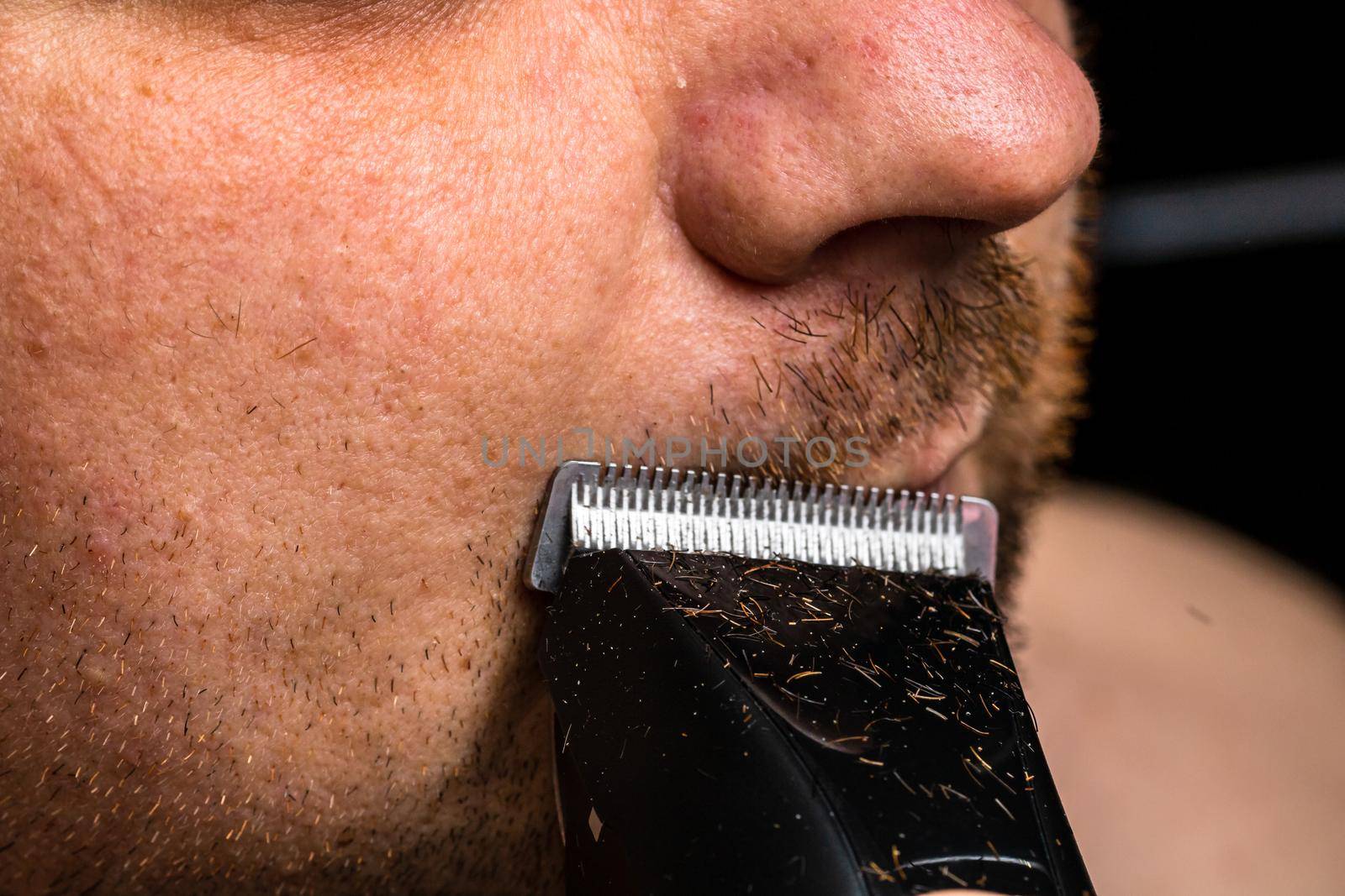 Man shaving or trimming his beard using a hair clipper by vladispas