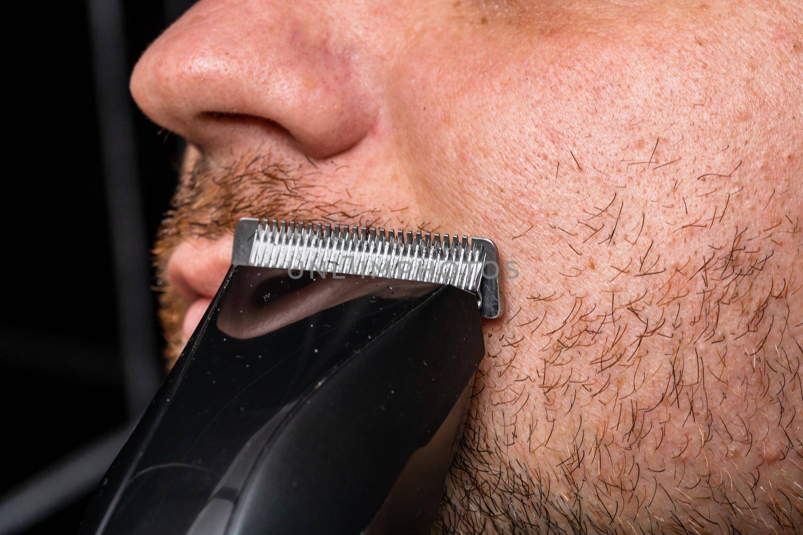 Man shaving or trimming his beard using a hair clipper by vladispas