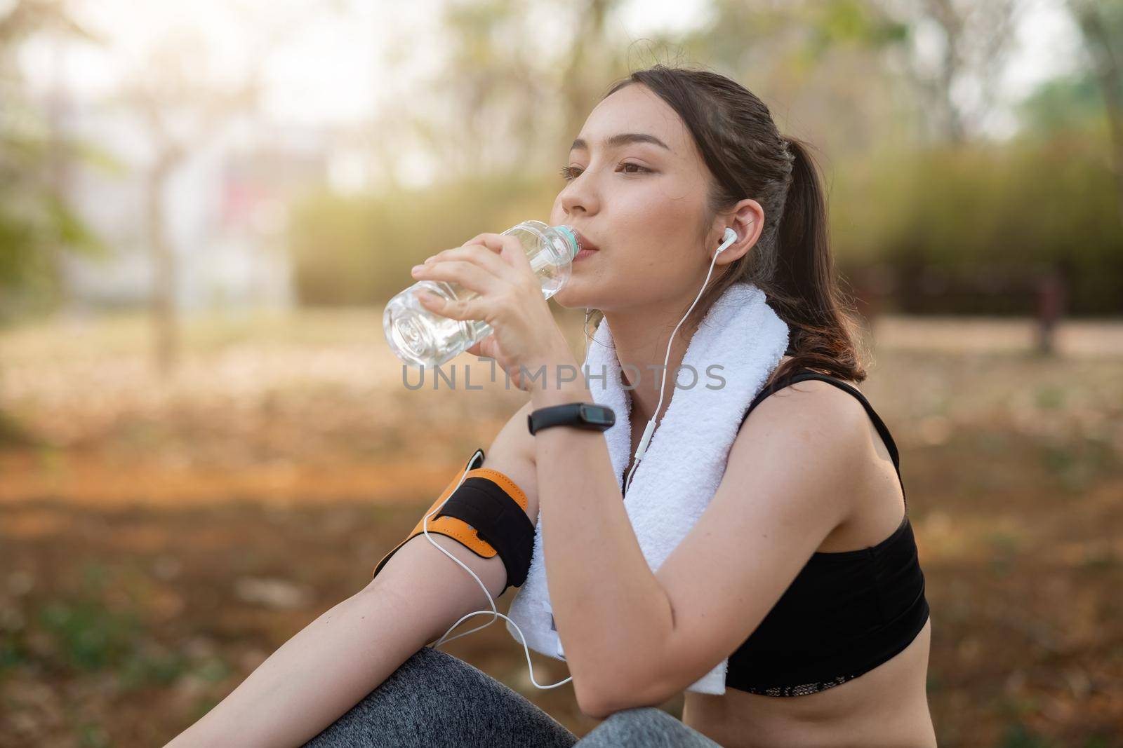 Young woman athlete takes a break, drinking water, out on a run on a hot day. by nateemee