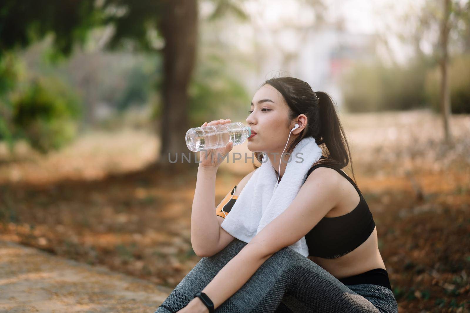 Young woman athlete takes a break, drinking water, out on a run on a hot day. by nateemee