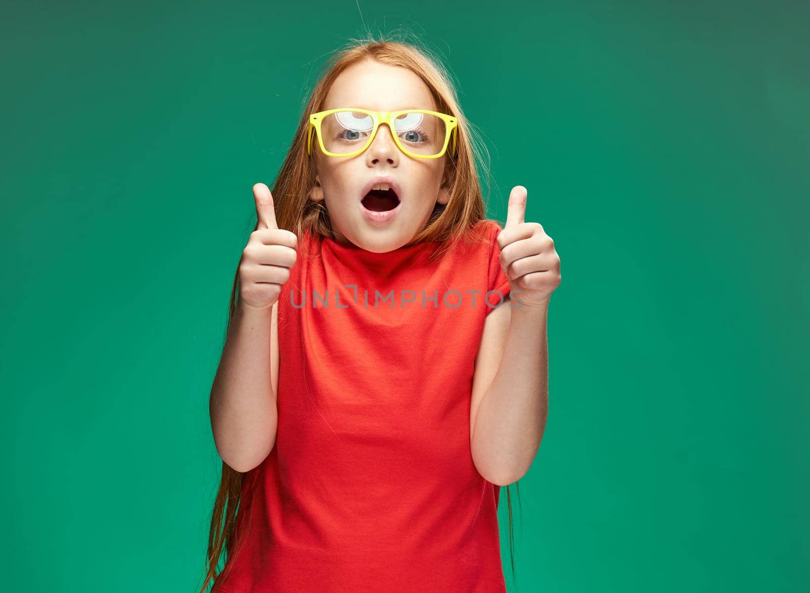 emotional red-haired girl in yellow glasses red t-shirt emotions studio green background. High quality photo