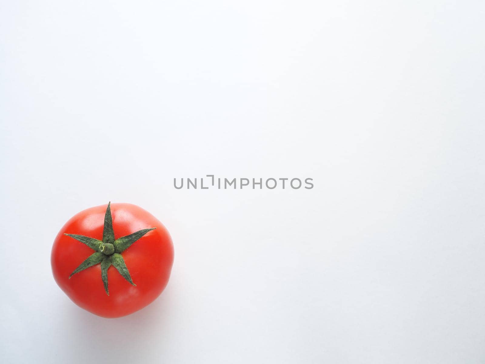 One red tomato on a white background is a close-up.