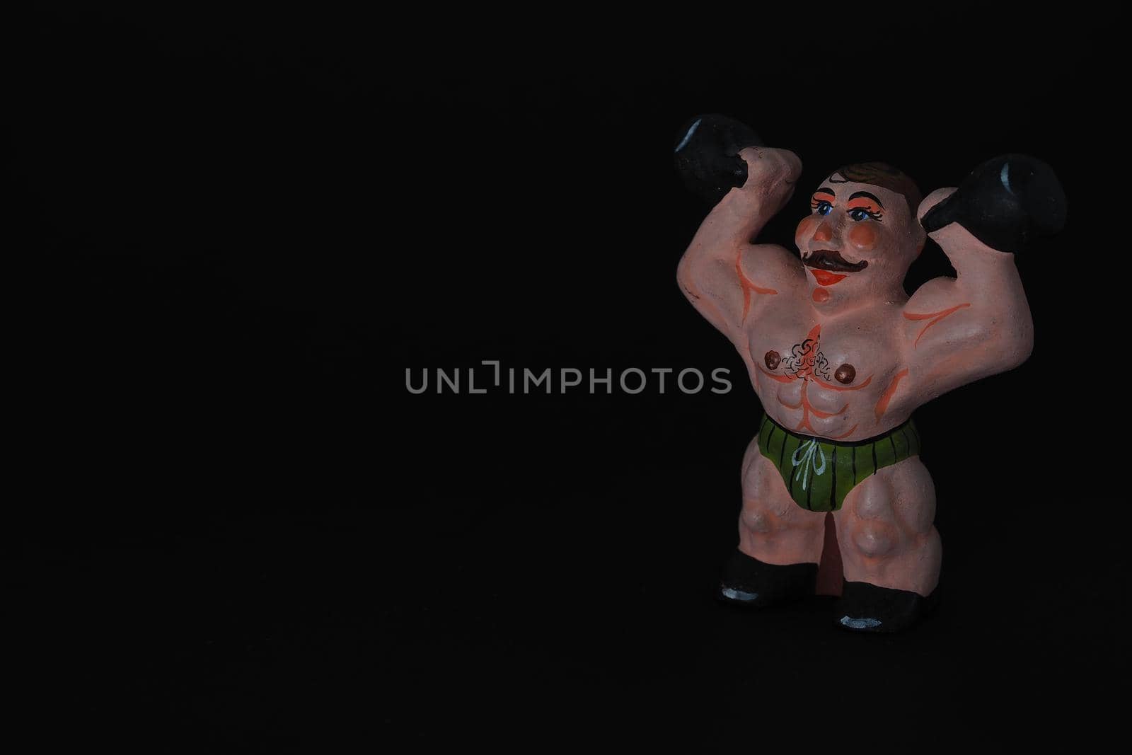 Athlete. Figures made of ceramics, plaster and clay. The man with the weights. Close-up. Black background.