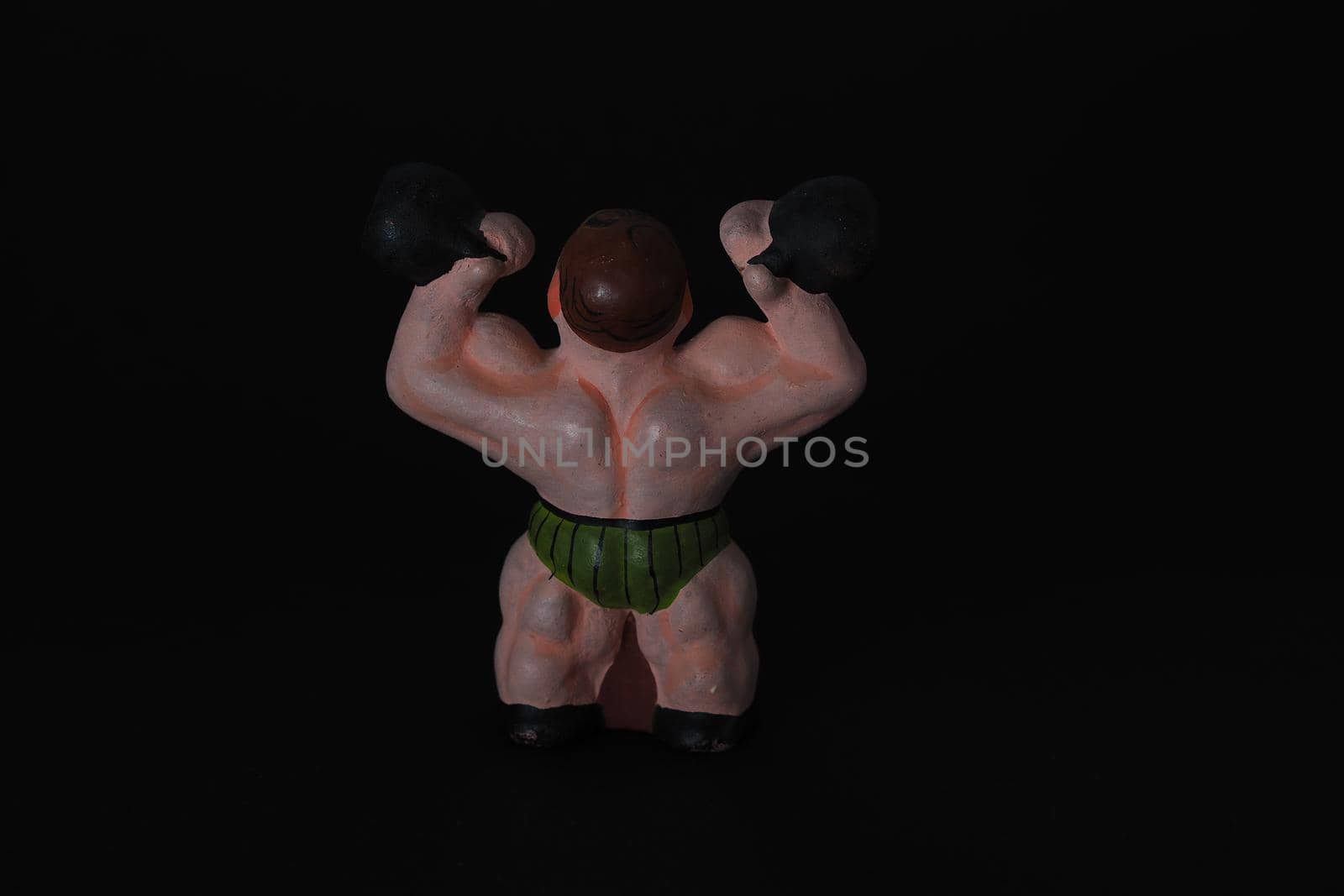 Athlete. Figures made of ceramics, plaster and clay. The man with the weights. Close-up. Black background.