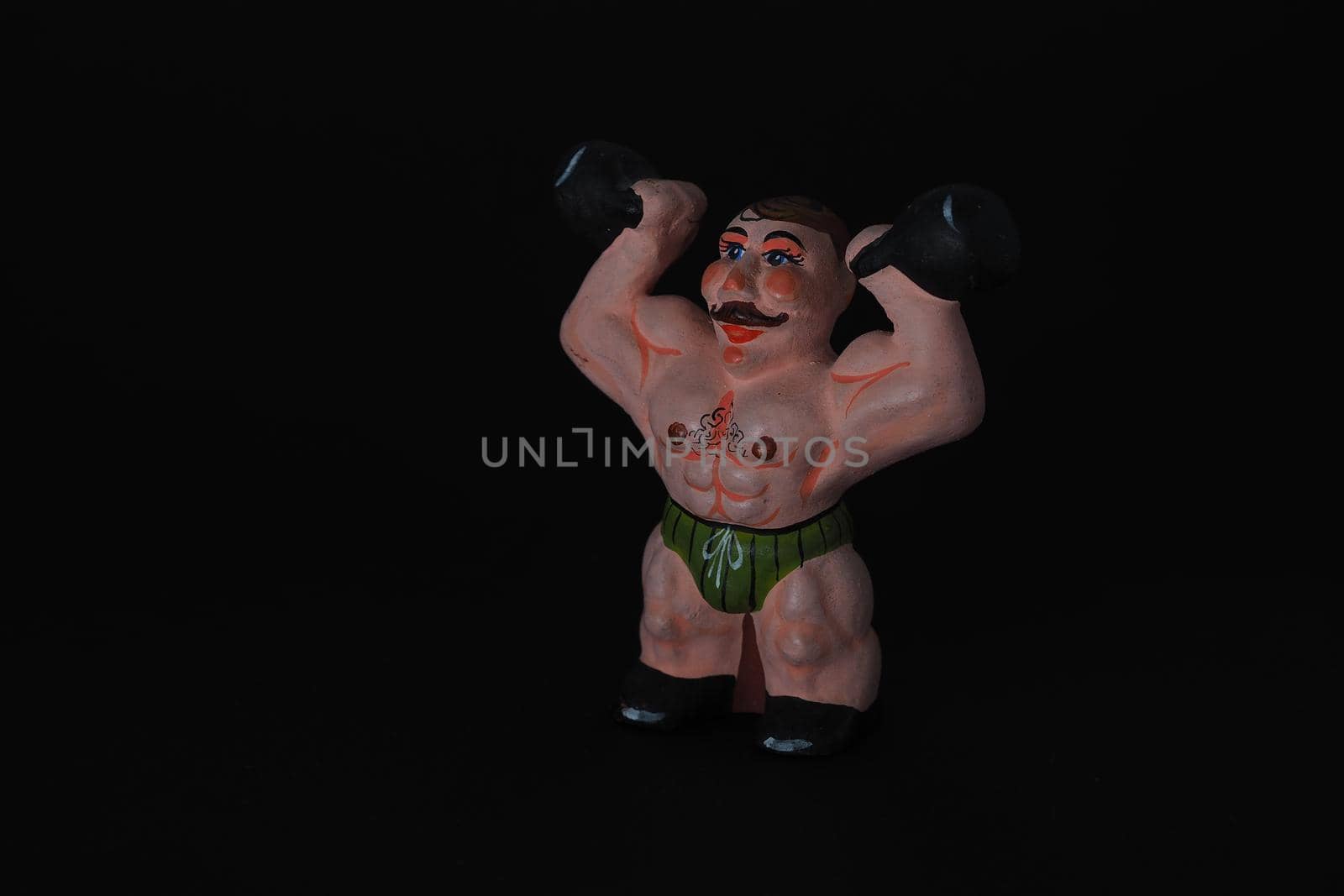 Athlete. Figures made of ceramics, plaster and clay. The man with the weights. Close-up. Black background.