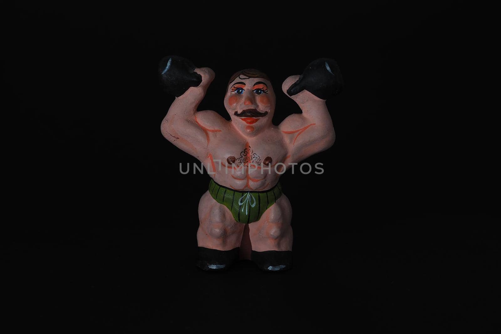 Athlete. Figures made of ceramics, plaster and clay. The man with the weights. Close-up. Black background.