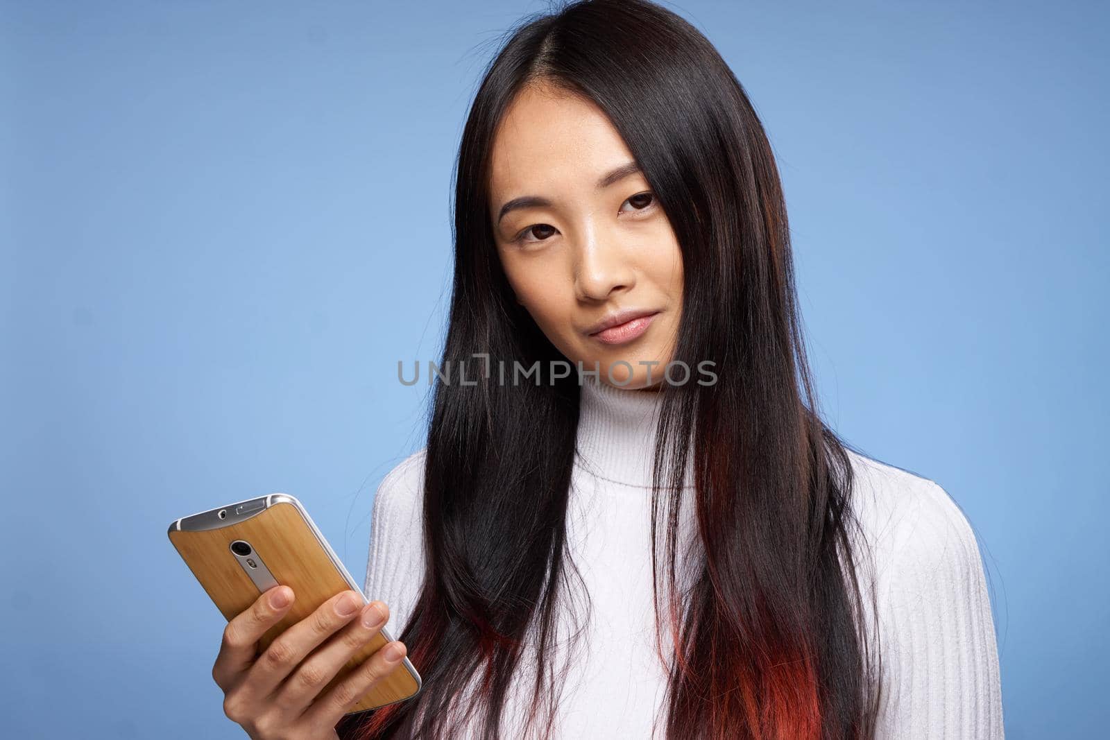 woman of asian appearance holding phone in hands internet communication technology blue background. High quality photo