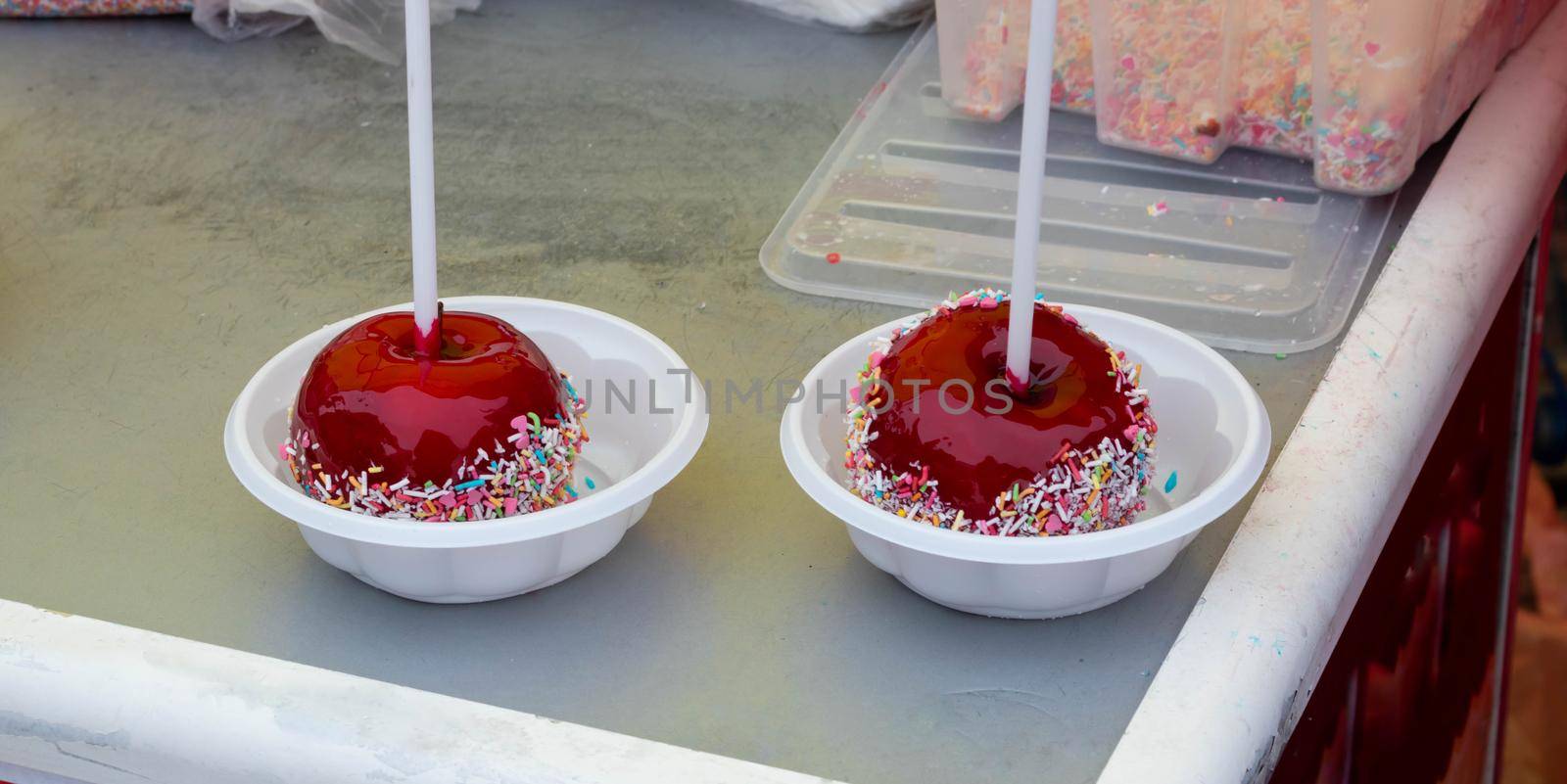 A red caramelized apple on a stick, covered in hard red sugar, standing in a plastic plate to serve as a festive treat. The concept of Easter, Maslenitsa,Valentine's Day.