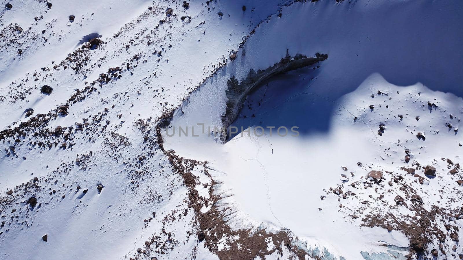 A huge wall of ice. Bogdanovich Glacier in the mountains of Almaty. The wind blows the snow away from the high frozen wave. Unusual shape and color of the ice. Moraine lake in winter in the mountains