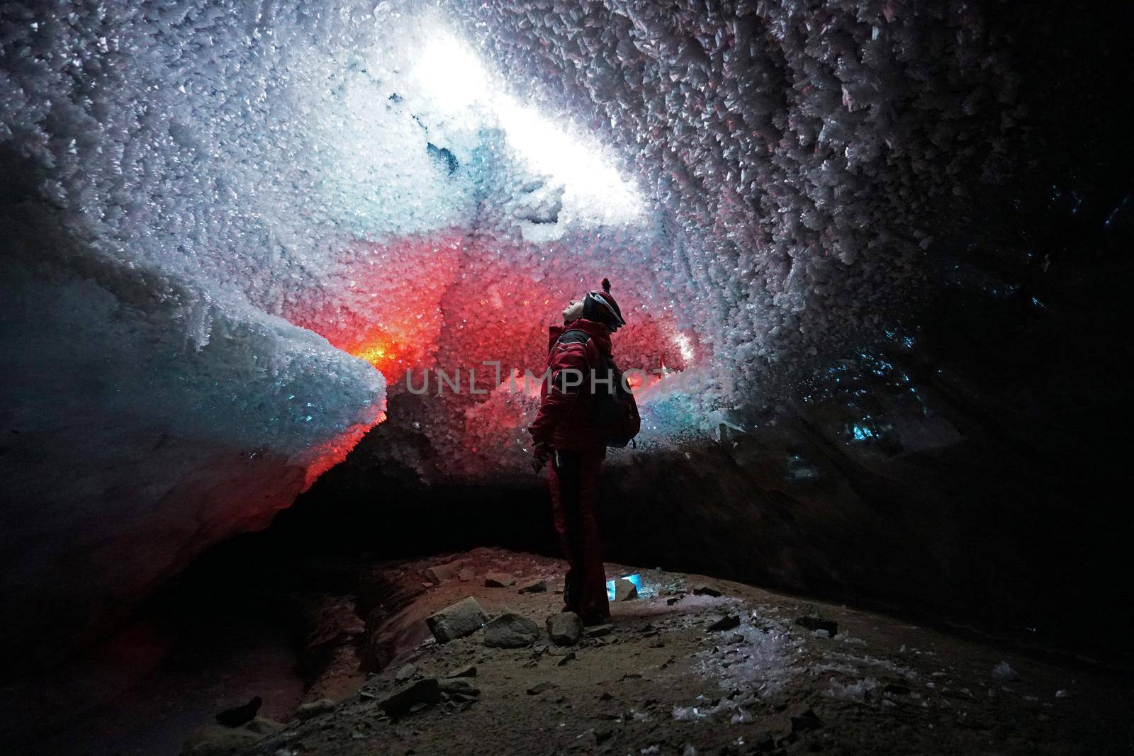 A guy in an ice cave with a lantern light. The caver descended into the ice cave. Snow stalactites and ice walls. In some places there are stones. Colored lantern beams. Bogdanovich Glacier, Almaty