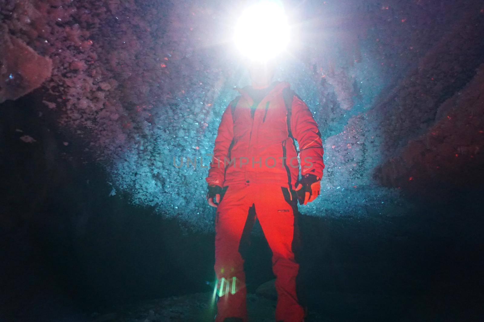 A guy in an ice cave with a lantern light. The caver descended into the ice cave. Snow stalactites and ice walls. In some places there are stones. Colored lantern beams. Bogdanovich Glacier, Almaty