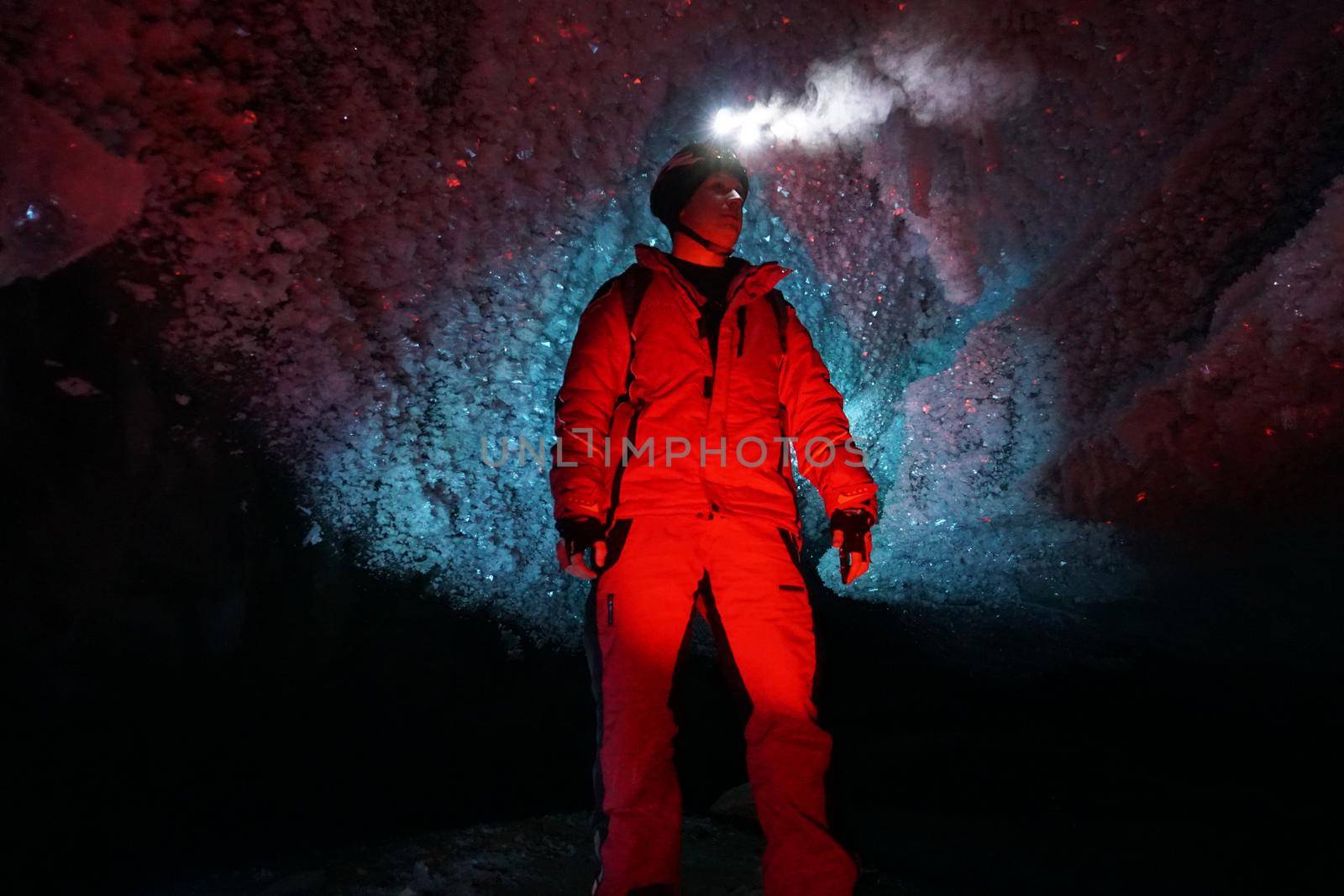 A guy in an ice cave with a lantern light. The caver descended into the ice cave. Snow stalactites and ice walls. In some places there are stones. Colored lantern beams. Bogdanovich Glacier, Almaty