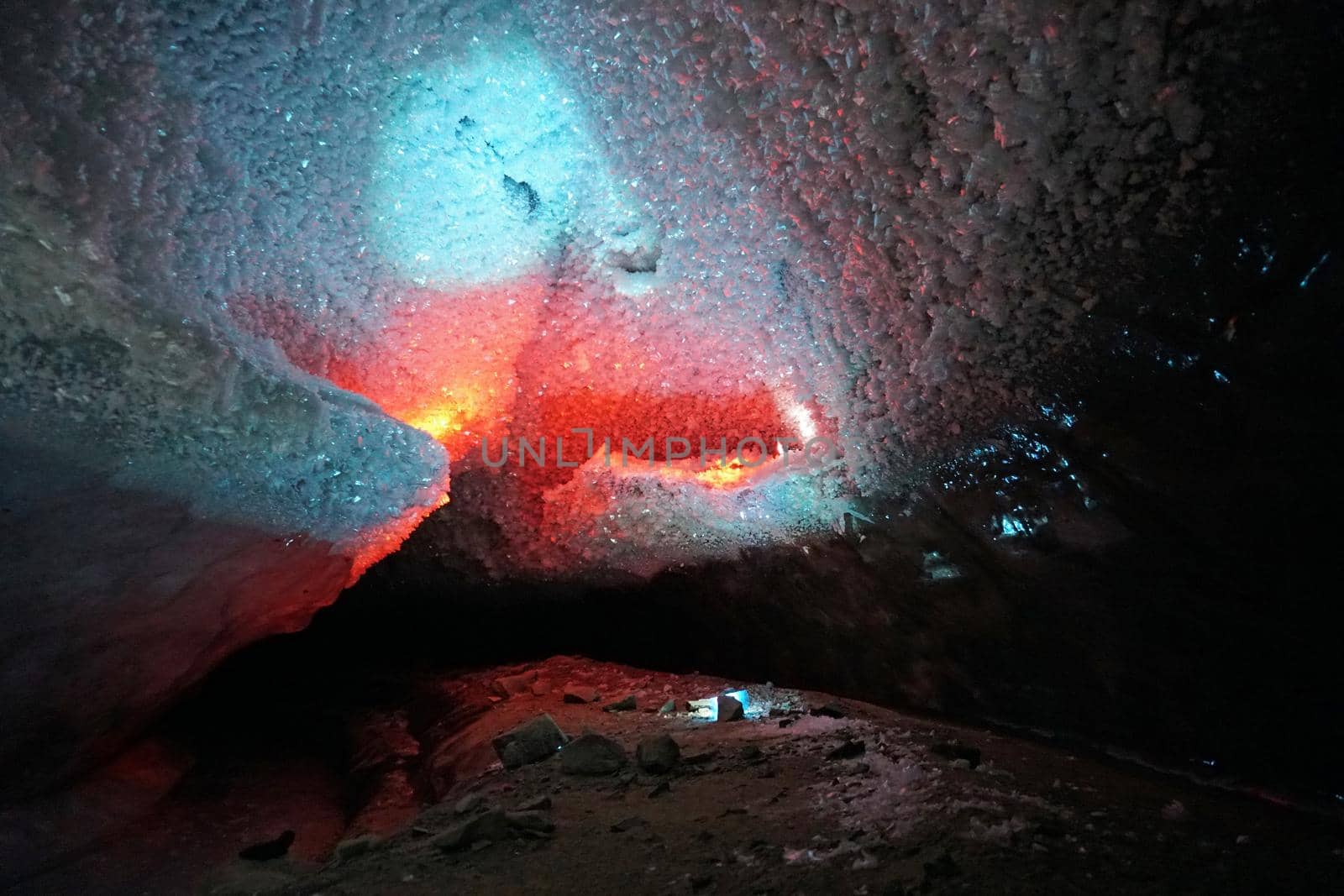 In an ice cave with colored lighting from lanterns. Snow and ice of interesting shapes grow on the walls of the cave. Stalactites hang. The huge ice walls shimmer with light. Macro photography. Almaty