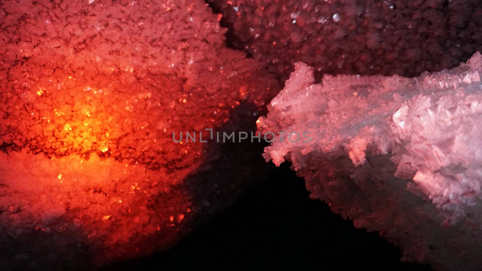 In an ice cave with colored lighting from lanterns. Snow and ice of interesting shapes grow on the walls of the cave. Stalactites hang. The huge ice walls shimmer with light. Macro photography. Almaty