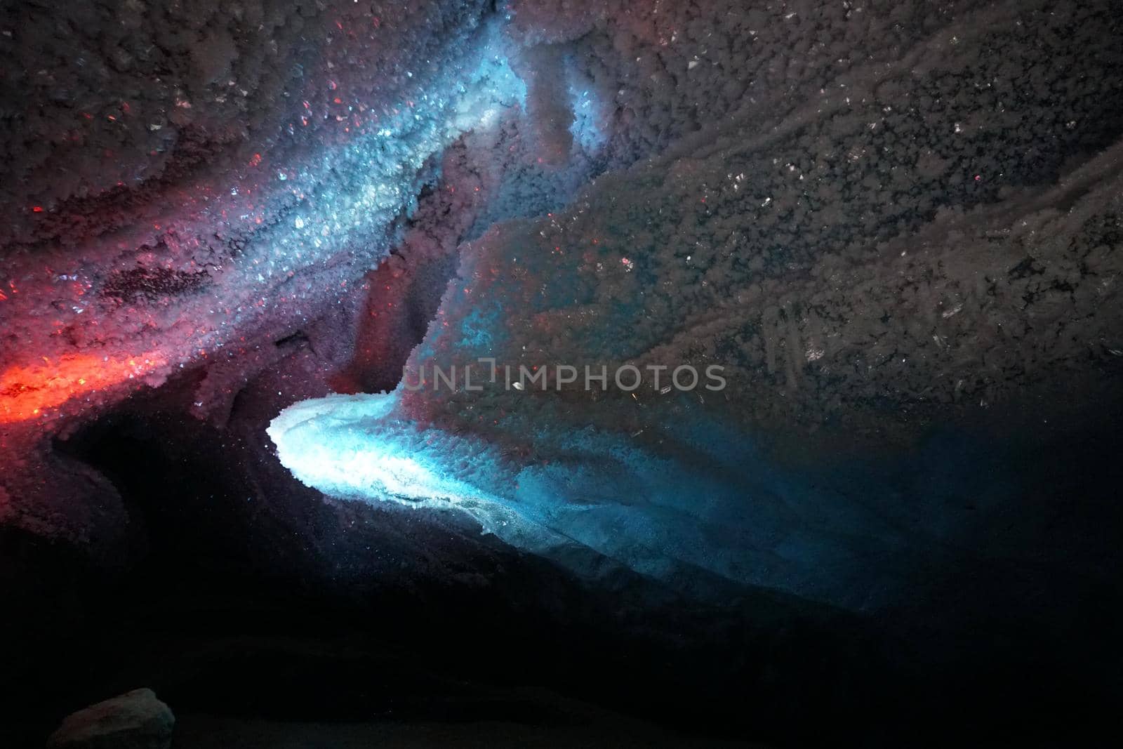 In an ice cave with colored lighting from lanterns. Snow and ice of interesting shapes grow on the walls of the cave. Stalactites hang. The huge ice walls shimmer with light. Macro photography. Almaty