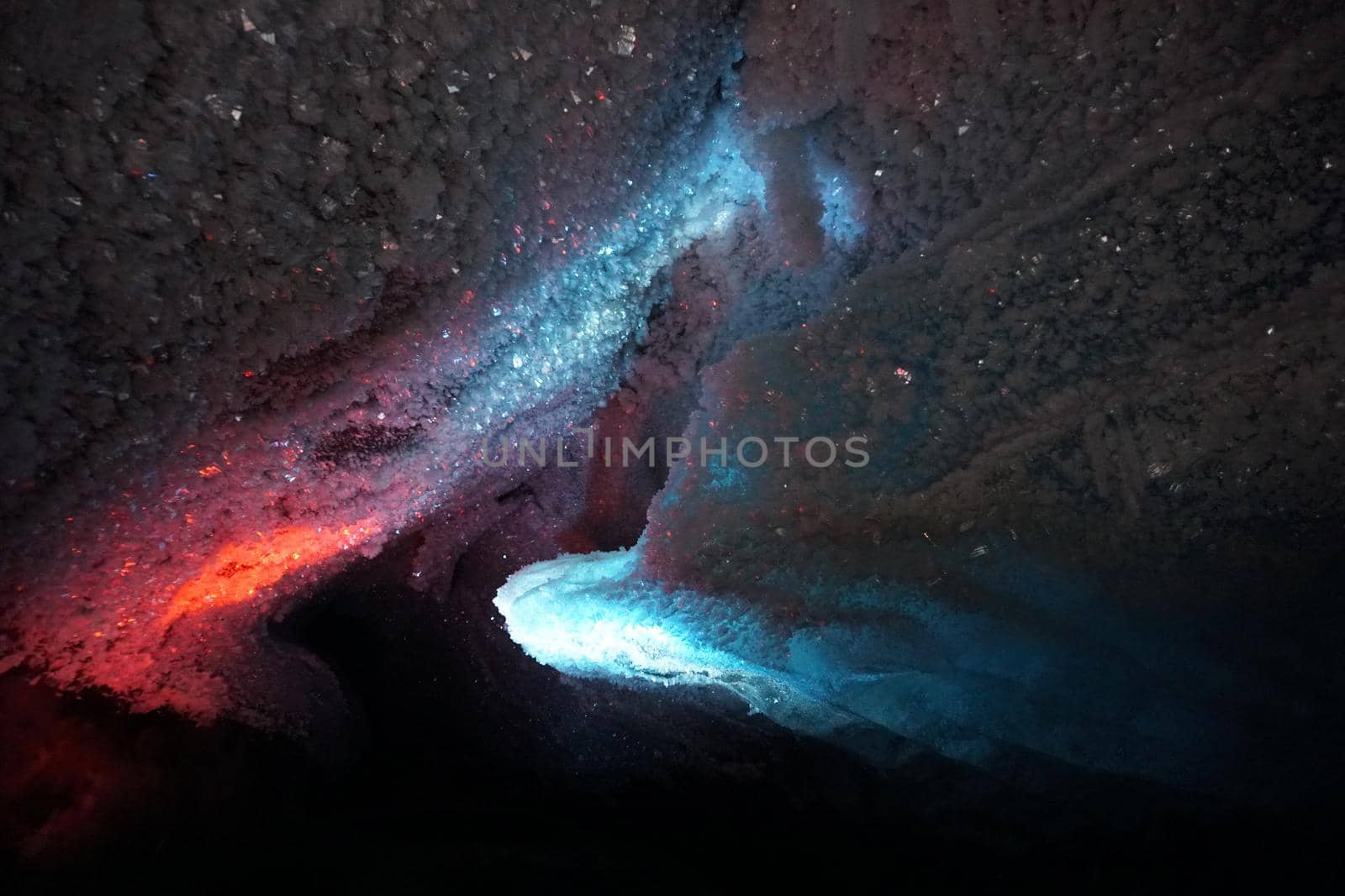 In an ice cave with colored lighting from lanterns. Snow and ice of interesting shapes grow on the walls of the cave. Stalactites hang. The huge ice walls shimmer with light. Macro photography. Almaty