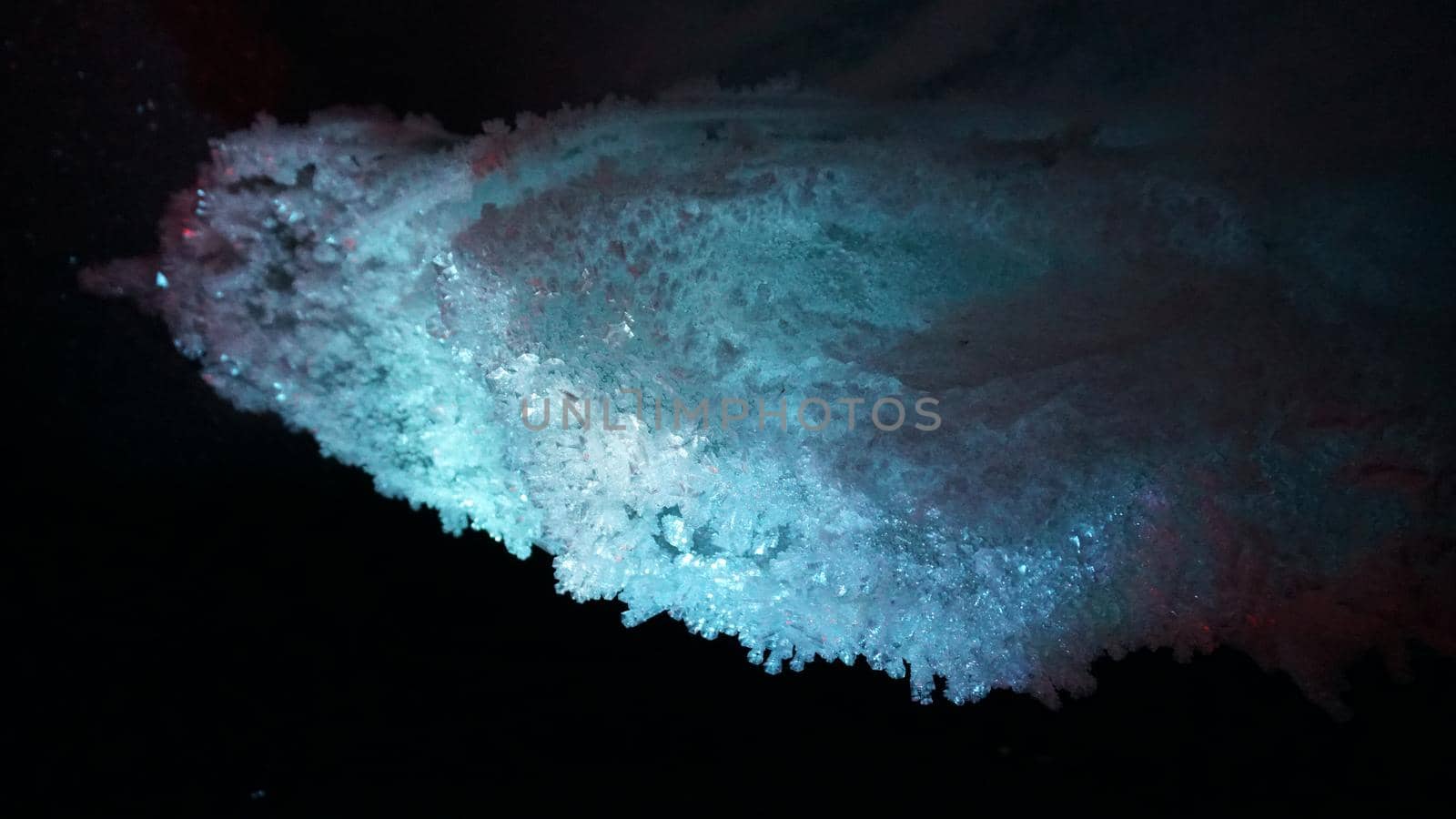 In an ice cave with colored lighting from lanterns. Snow and ice of interesting shapes grow on the walls of the cave. Stalactites hang. The huge ice walls shimmer with light. Macro photography. Almaty