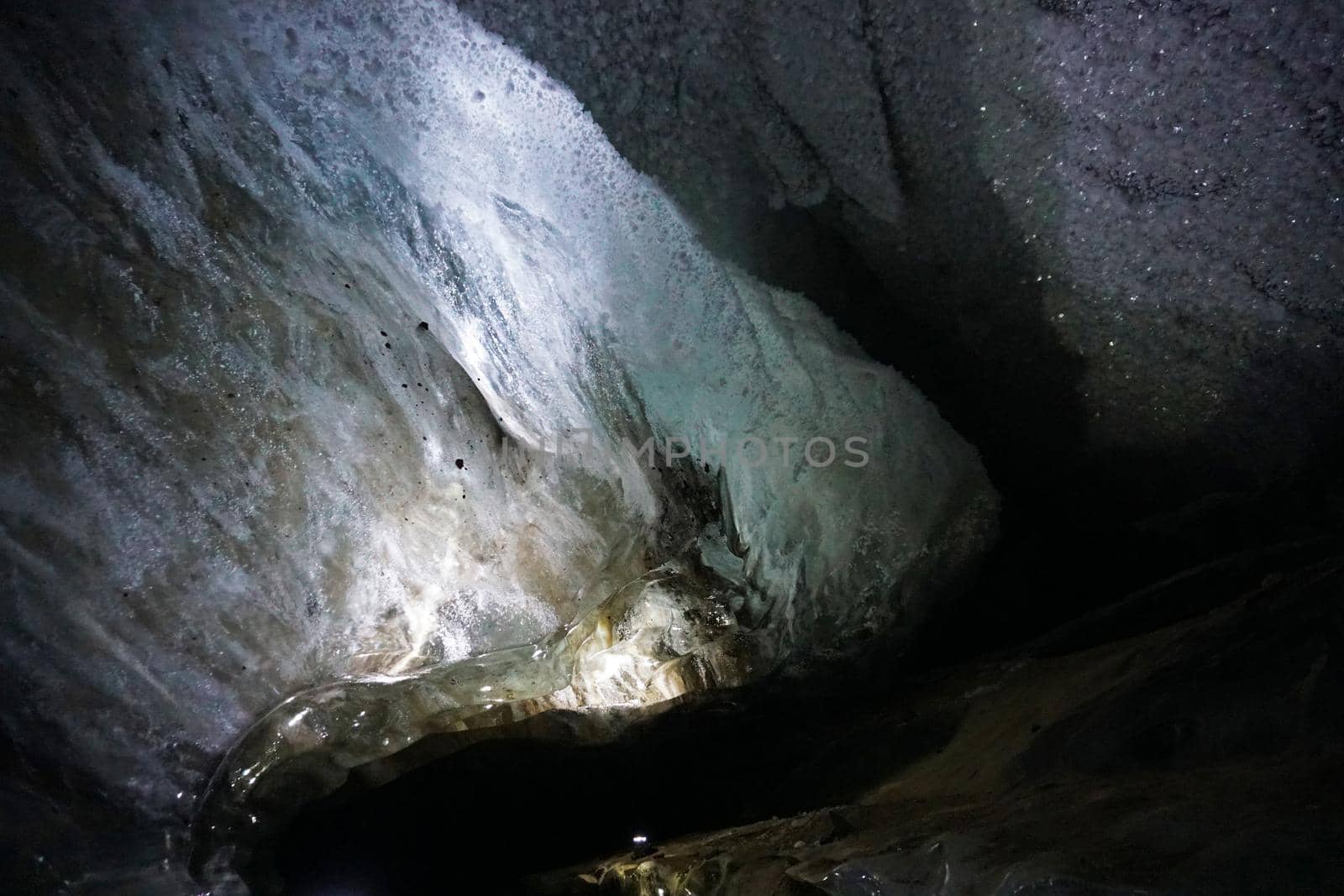 In an ice cave with colored lighting from lanterns. Snow and ice of interesting shapes grow on the walls of the cave. Stalactites hang. The huge ice walls shimmer with light. Macro photography. Almaty