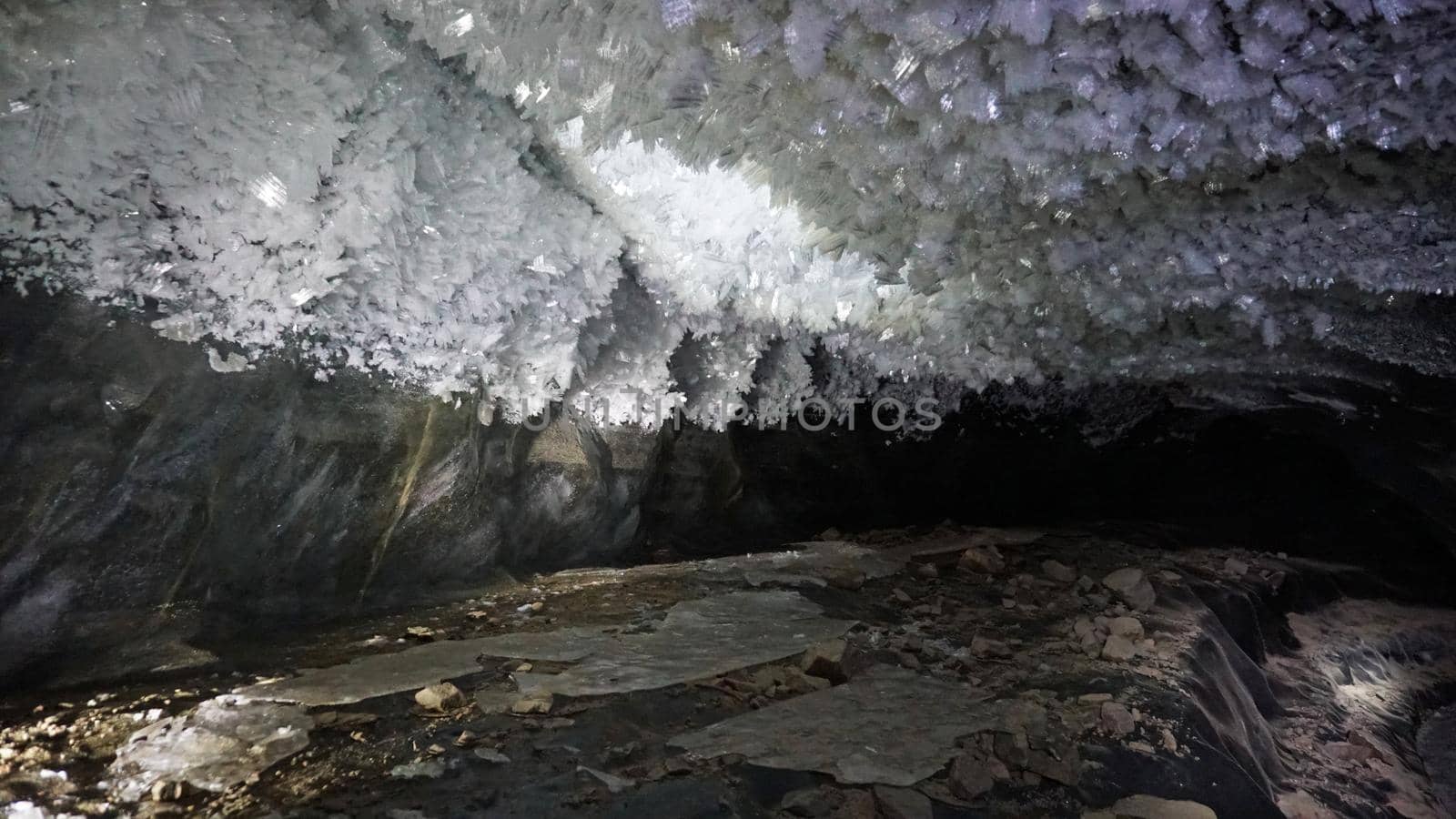 In an ice cave with colored lighting from lanterns. Snow and ice of interesting shapes grow on the walls of the cave. Stalactites hang. The huge ice walls shimmer with light. Macro photography. Almaty