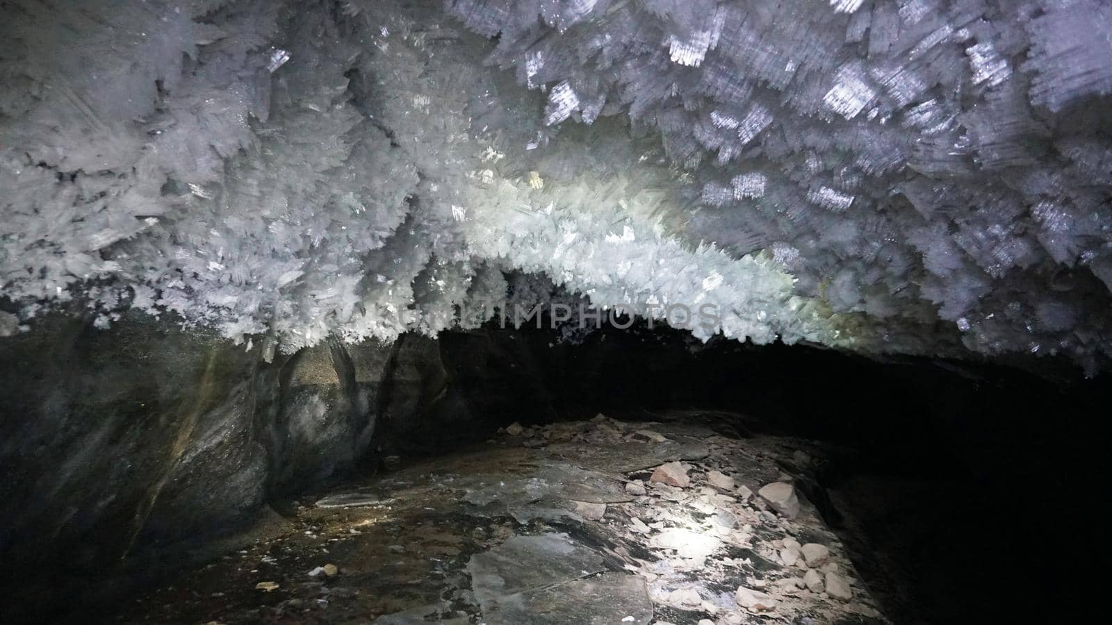 In an ice cave with colored lighting from lanterns. Snow and ice of interesting shapes grow on the walls of the cave. Stalactites hang. The huge ice walls shimmer with light. Macro photography. Almaty