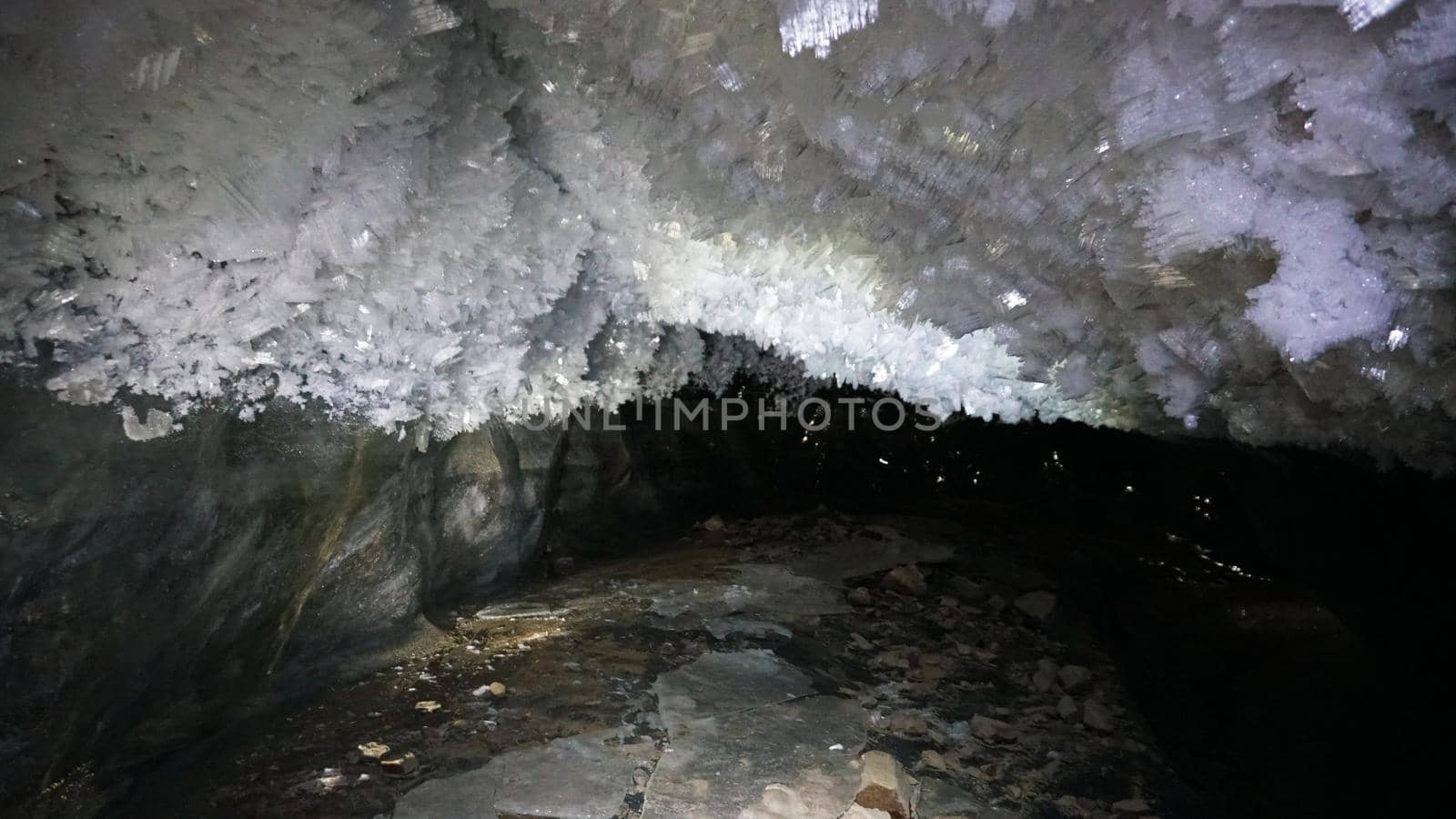 In an ice cave with colored lighting from lanterns. Snow and ice of interesting shapes grow on the walls of the cave. Stalactites hang. The huge ice walls shimmer with light. Macro photography. Almaty