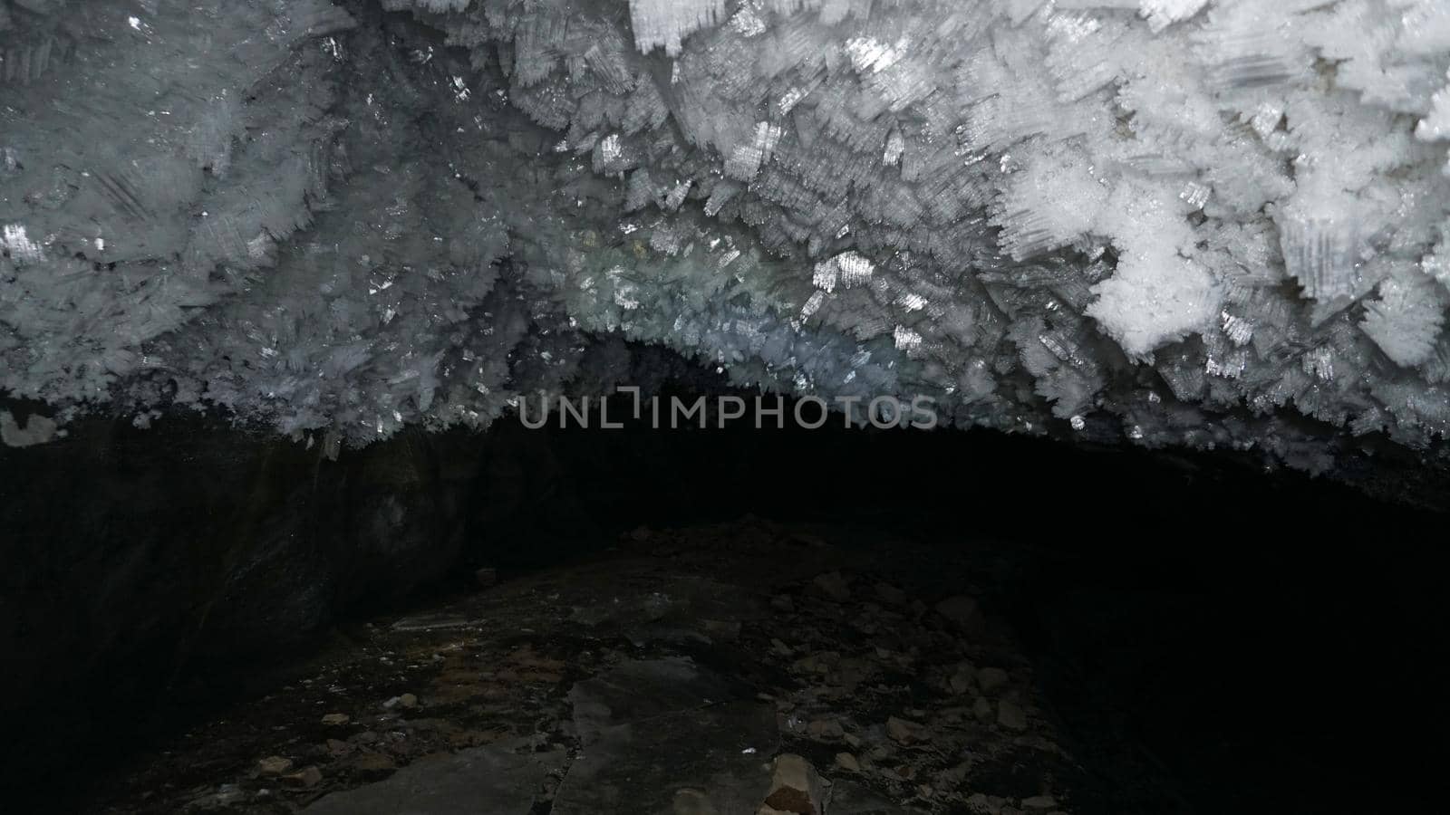 In an ice cave with colored lighting from lanterns. Snow and ice of interesting shapes grow on the walls of the cave. Stalactites hang. The huge ice walls shimmer with light. Macro photography. Almaty