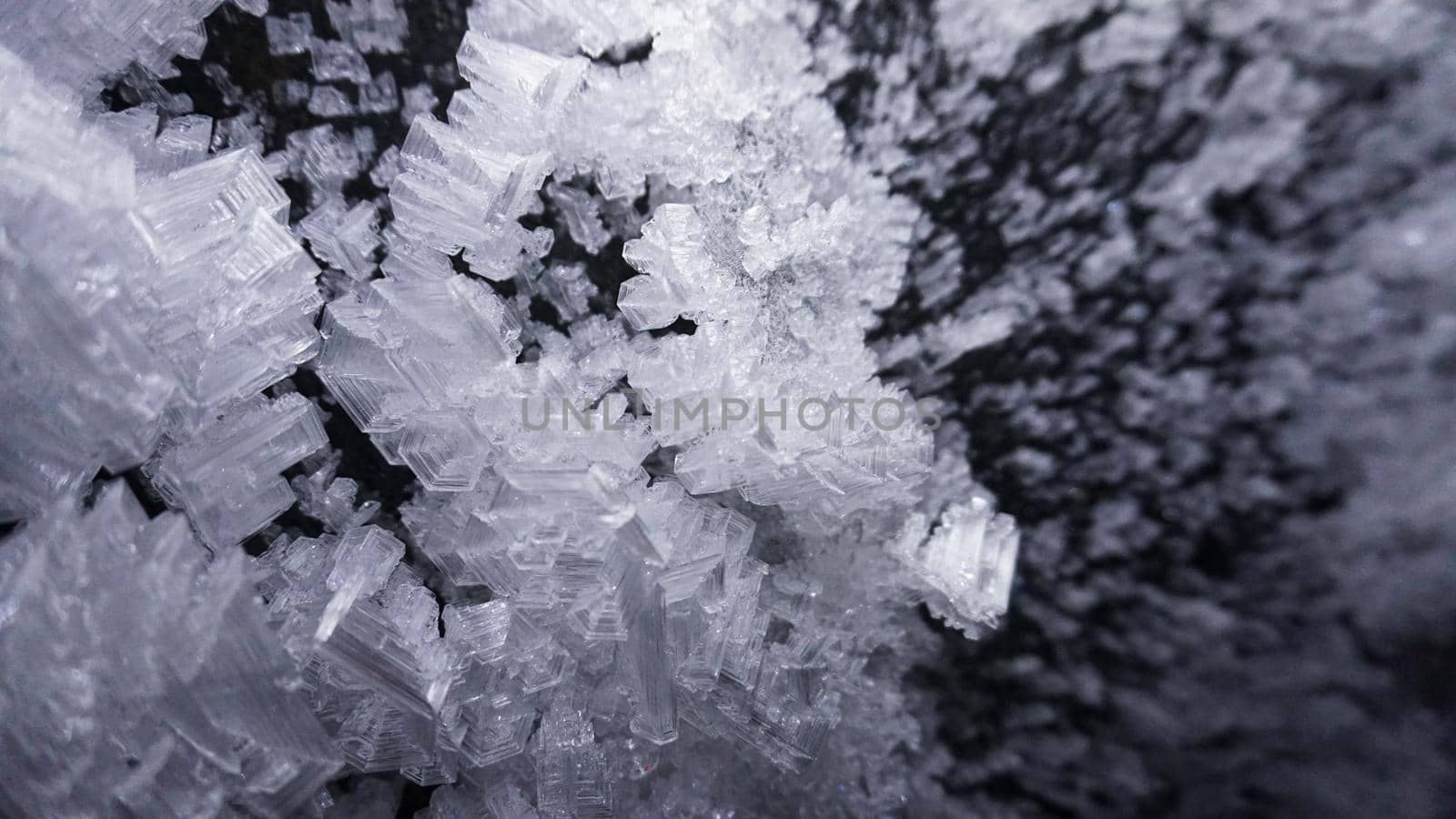 Macro photography of ice growths in a cave. Snow and ice of interesting shapes grow on the walls of the cave. Stalactites hang. Huge ice walls shimmer from the light of the lantern. Almaty, Kazakhstan