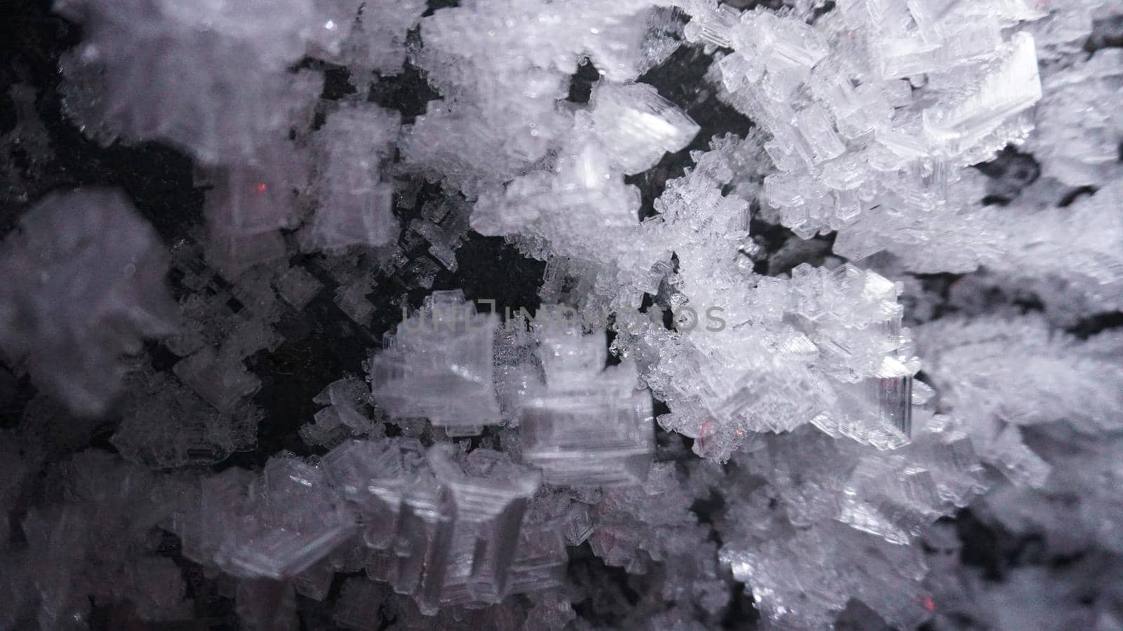 Macro photography of ice growths in a cave. Snow and ice of interesting shapes grow on the walls of the cave. Stalactites hang. Huge ice walls shimmer from the light of the lantern. Almaty, Kazakhstan