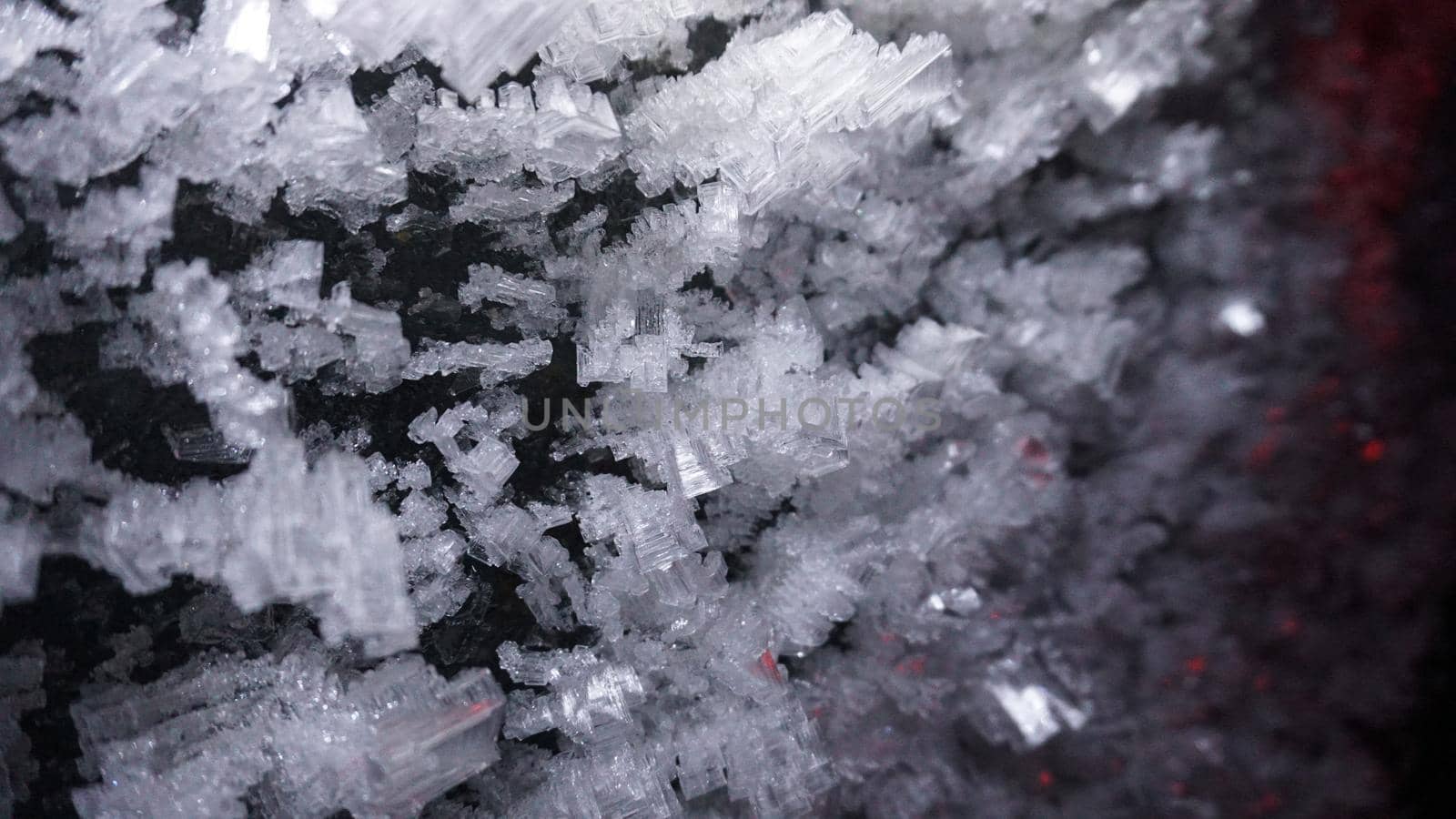 Macro photography of ice growths in a cave. Snow and ice of interesting shapes grow on the walls of the cave. Stalactites hang. Huge ice walls shimmer from the light of the lantern. Almaty, Kazakhstan